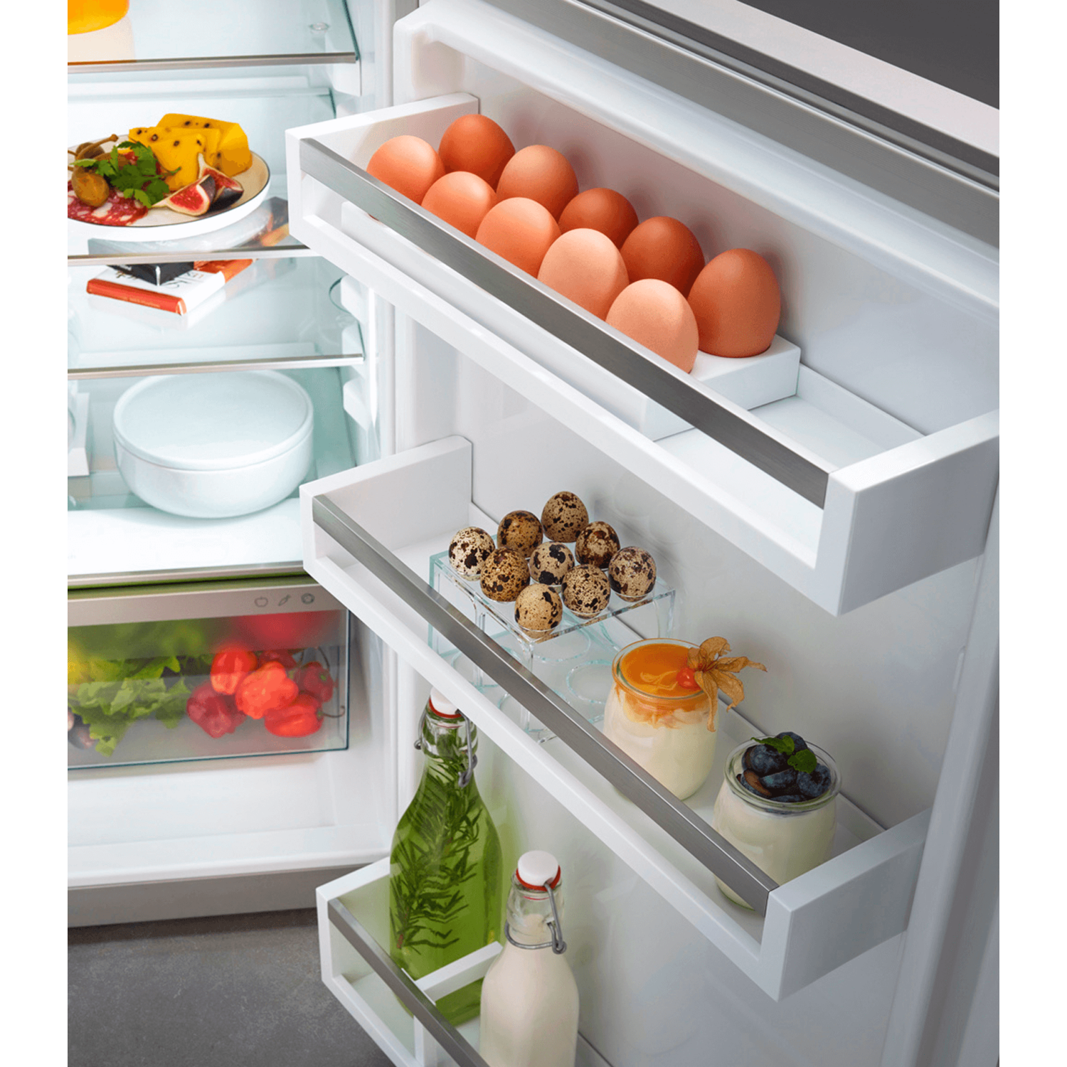 Refrigerator interior with shelves holding eggs, quail eggs, yogurt, and other food items. Glass bottles are also there.