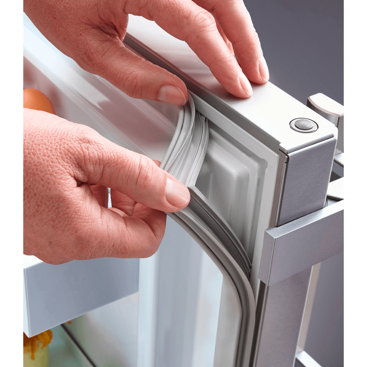 Hands removing a gray rubber seal from a refrigerator door, revealing the inner lining.