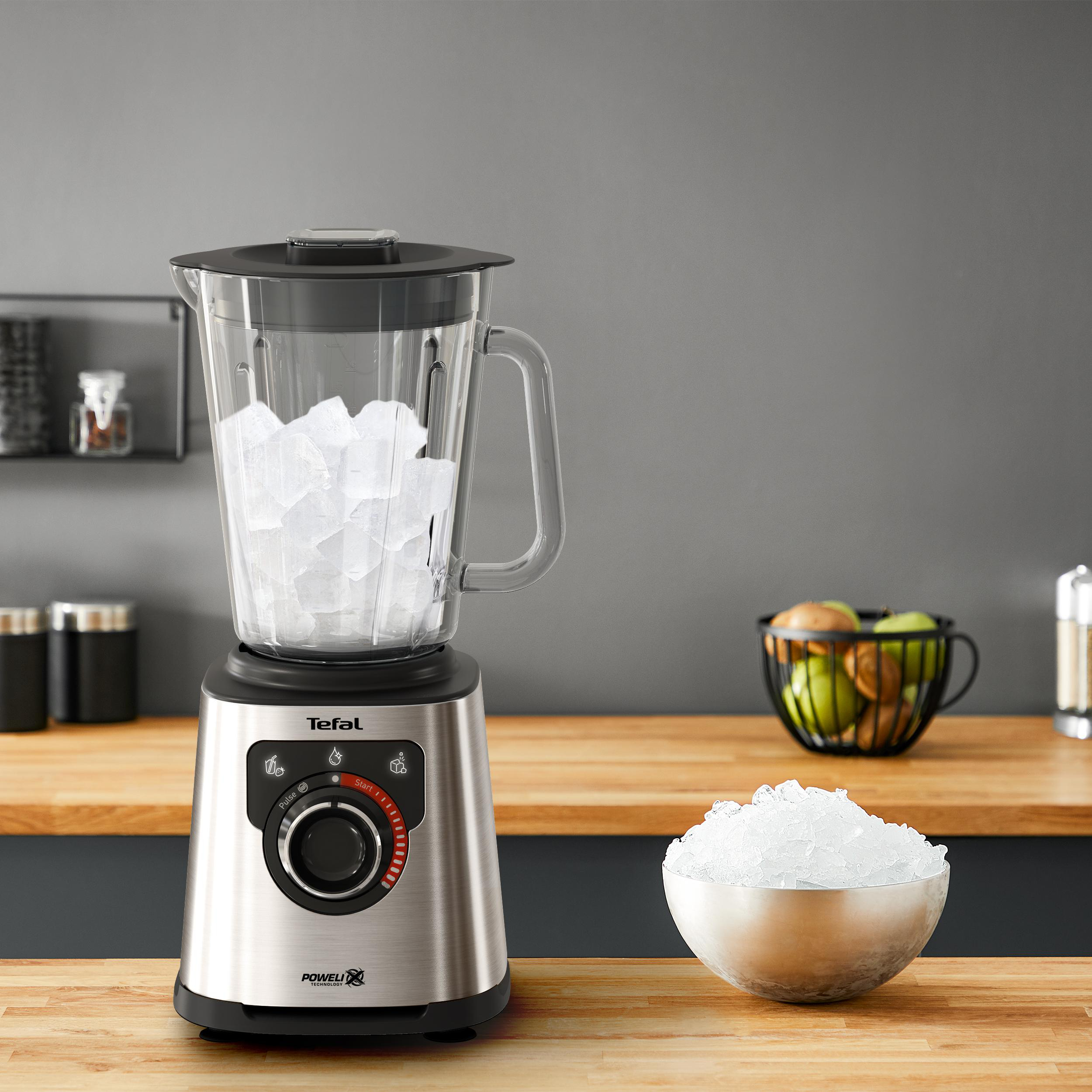 Ein Edelstahl-Mixer mit Eis im Glas, eine Schüssel mit Eis und ein Obstkorb.