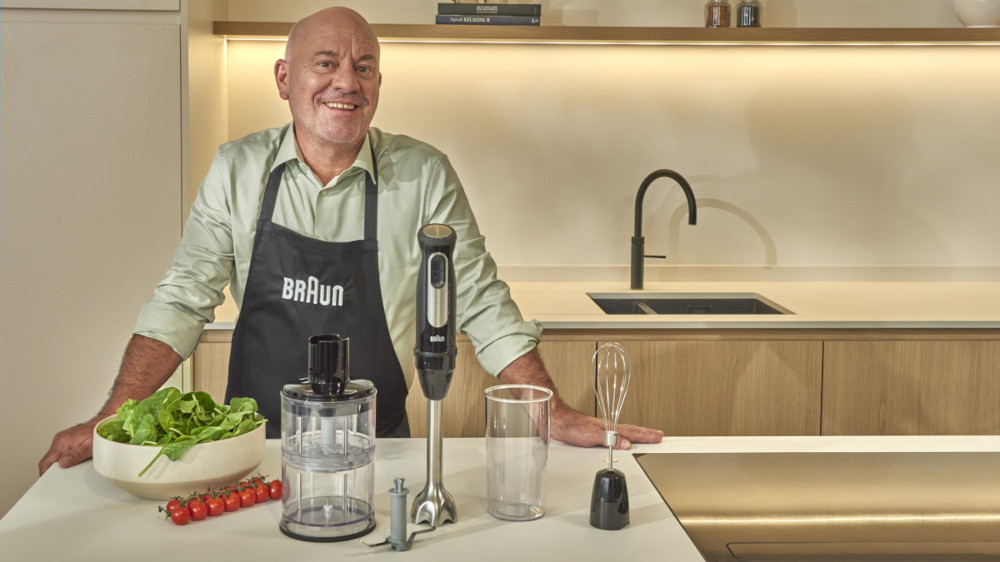 Man in kitchen with blender and ingredients.