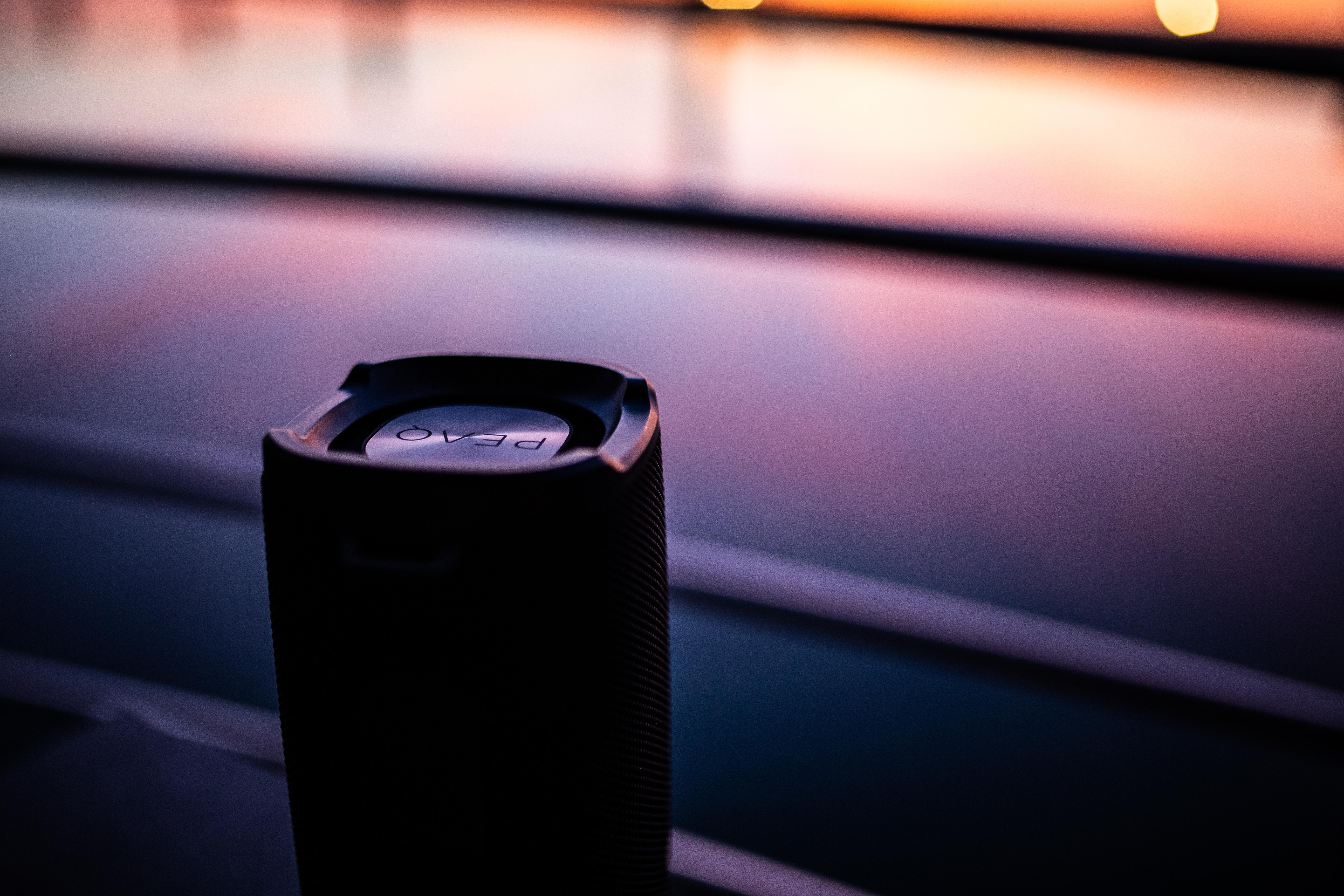 Schwarzer Lautsprecher auf reflektierender Oberfläche mit verschwommenem Hintergrund. Sonnenuntergang.