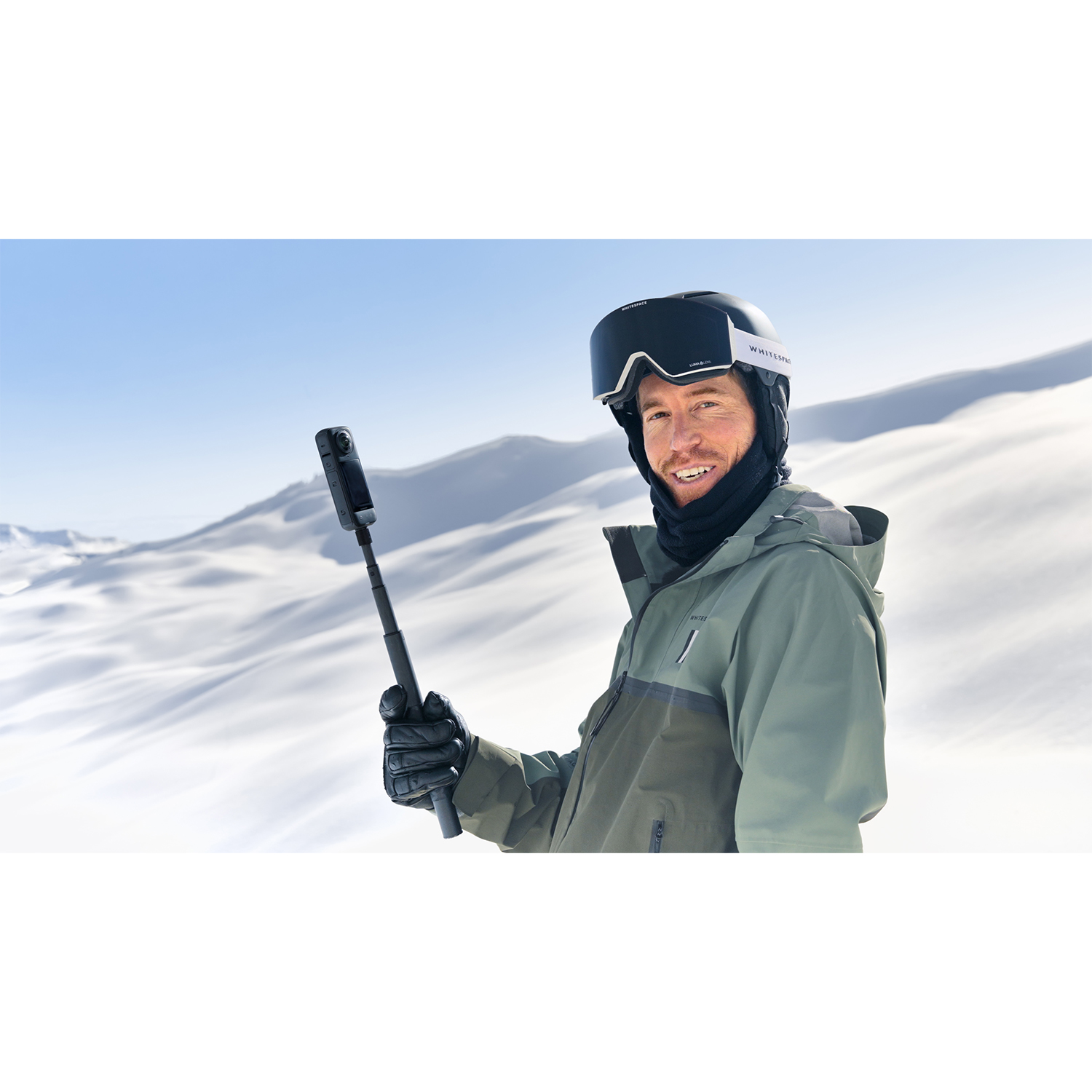 Uomo in abbigliamento da sci con una fotocamera su un bastone per selfie sullo sfondo.