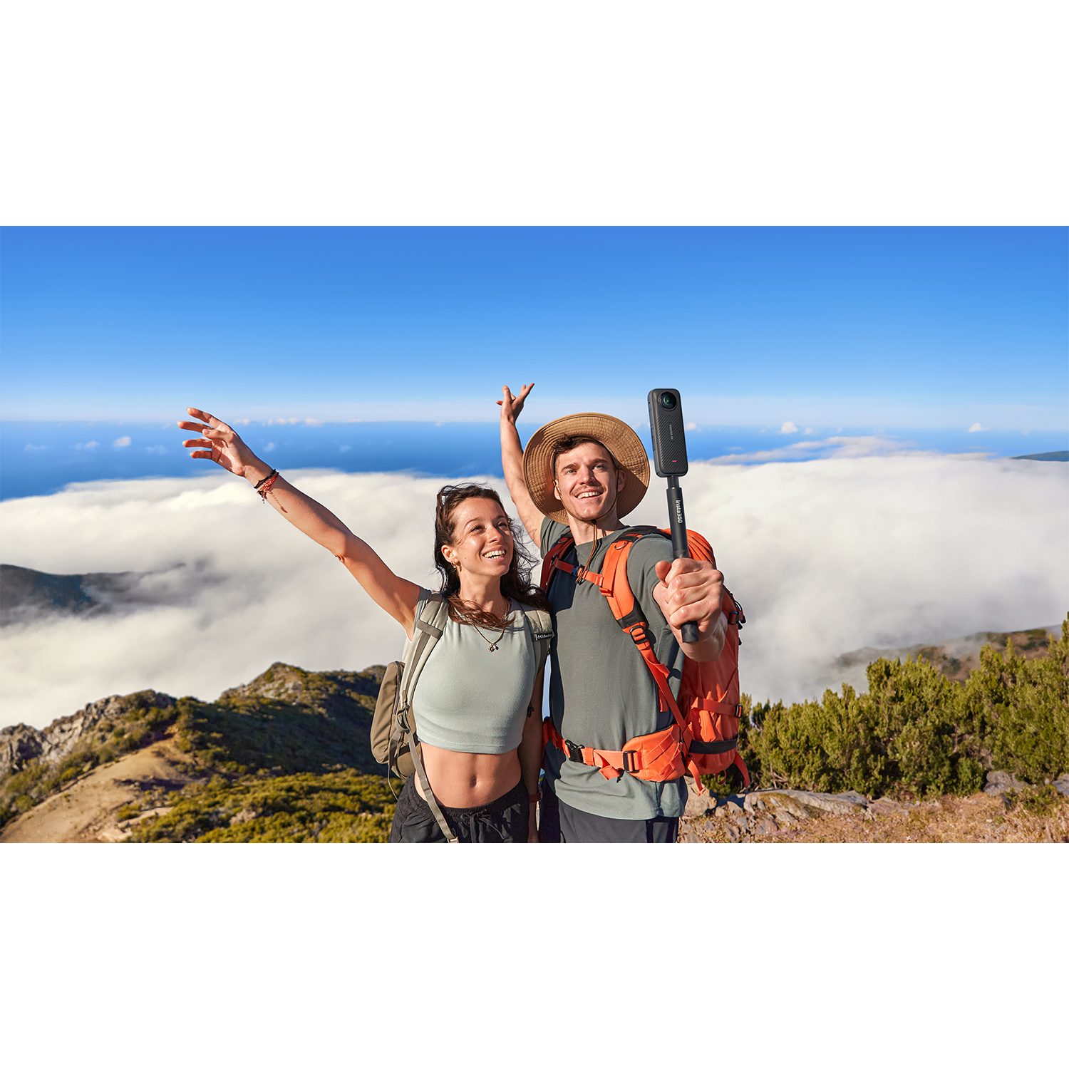 Due persone sulla cima di una montagna, una con una fotocamera su un bastone, con nuvole sotto.