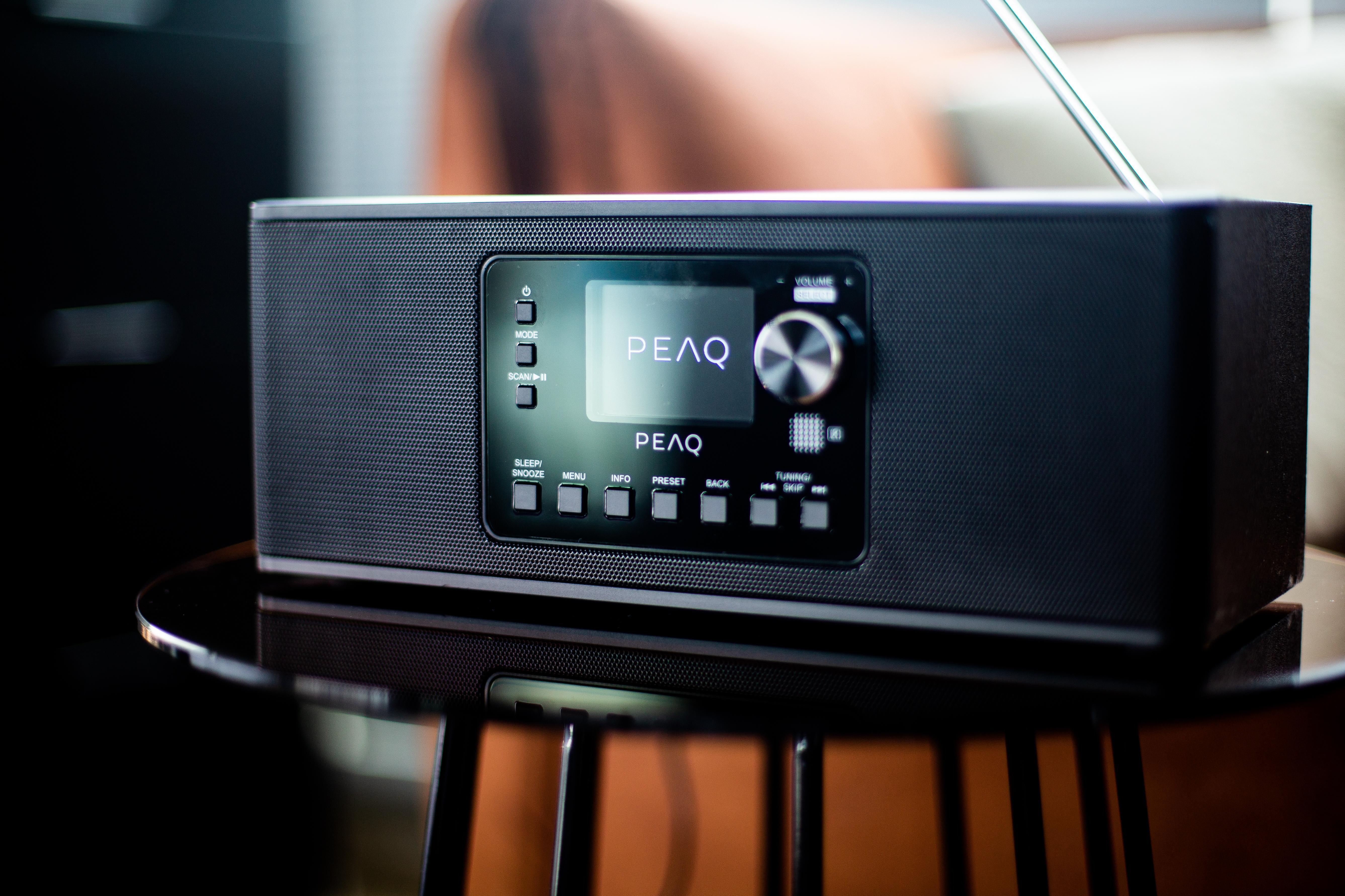 Schwarzes PEAQ-Radio auf einem Tisch. Display zeigt PEAQ-Logo und Tasten.
