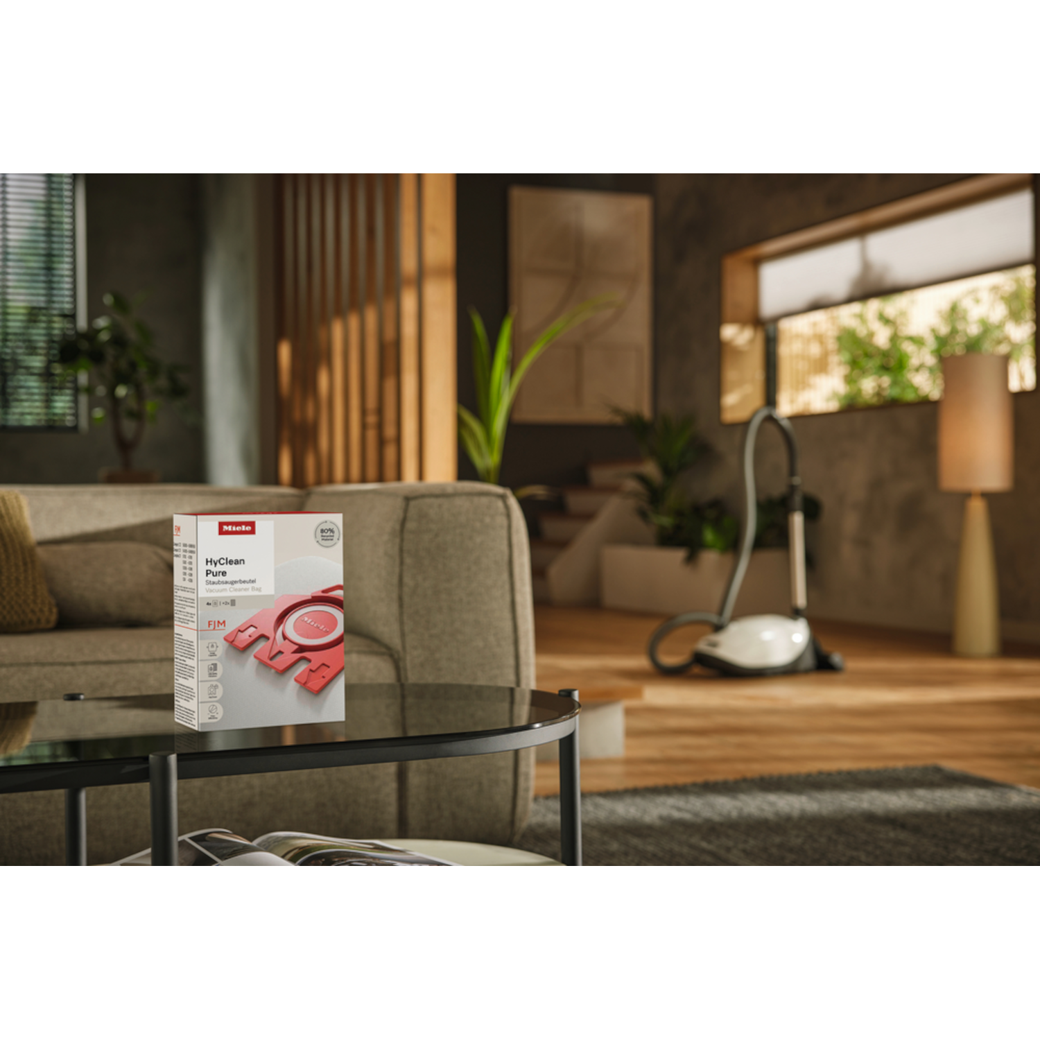 A living room with a box of vacuum cleaner bags on a table. A vacuum cleaner is in the background near a window.