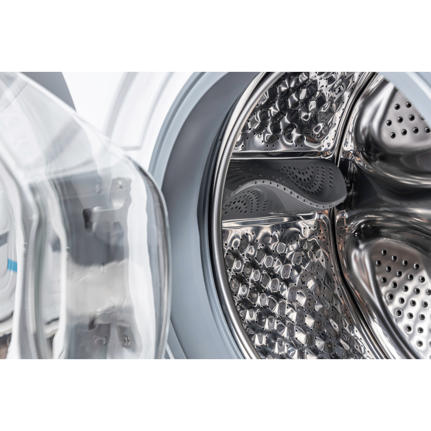 Washing machine drum with the door open. Shiny metal interior with holes, clear door panel.