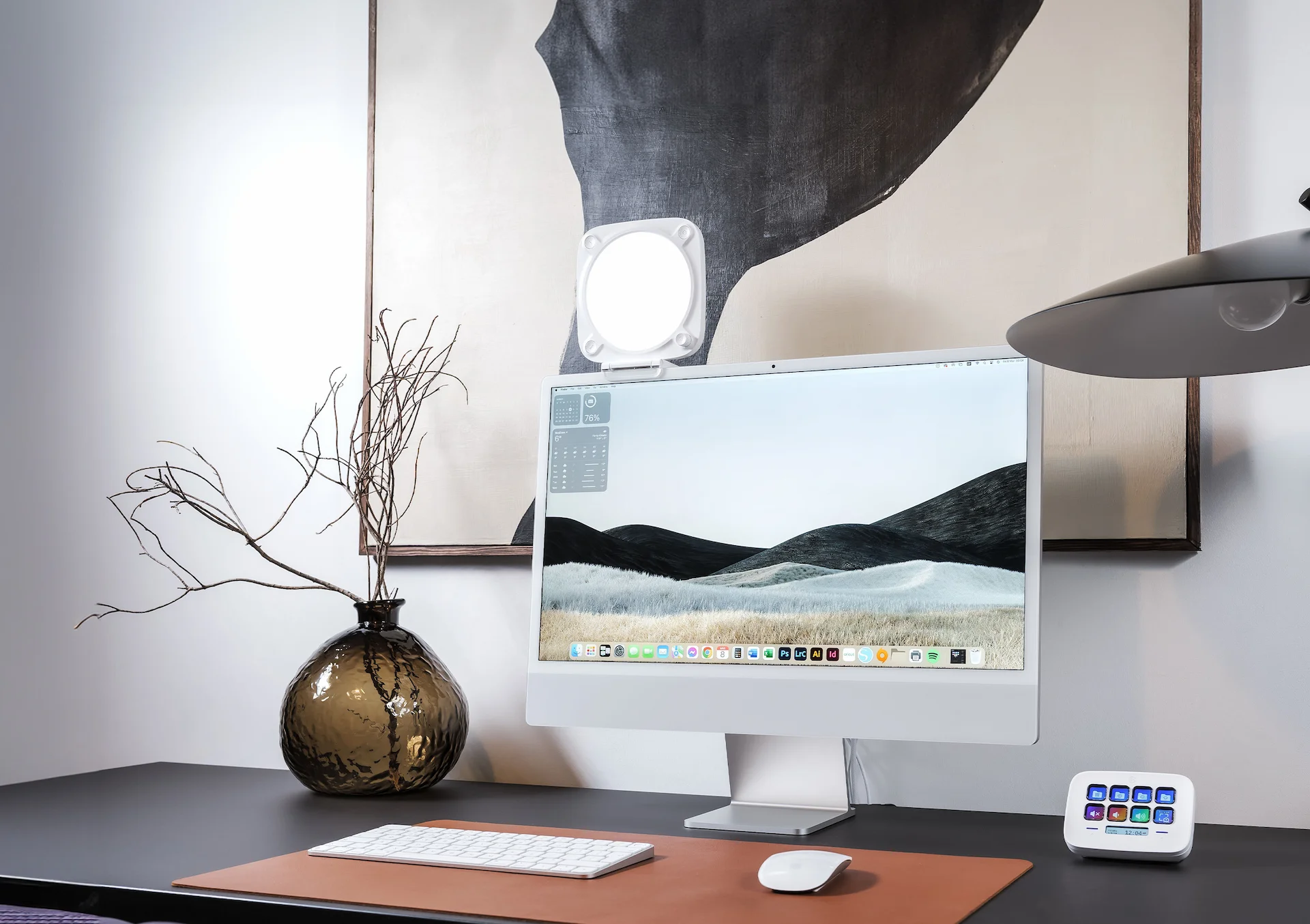 Computer-Setup auf einem Schreibtisch. Ein weißer iMac, Monitorlicht, Tastatur, Maus und eine Vase mit Pflanze.