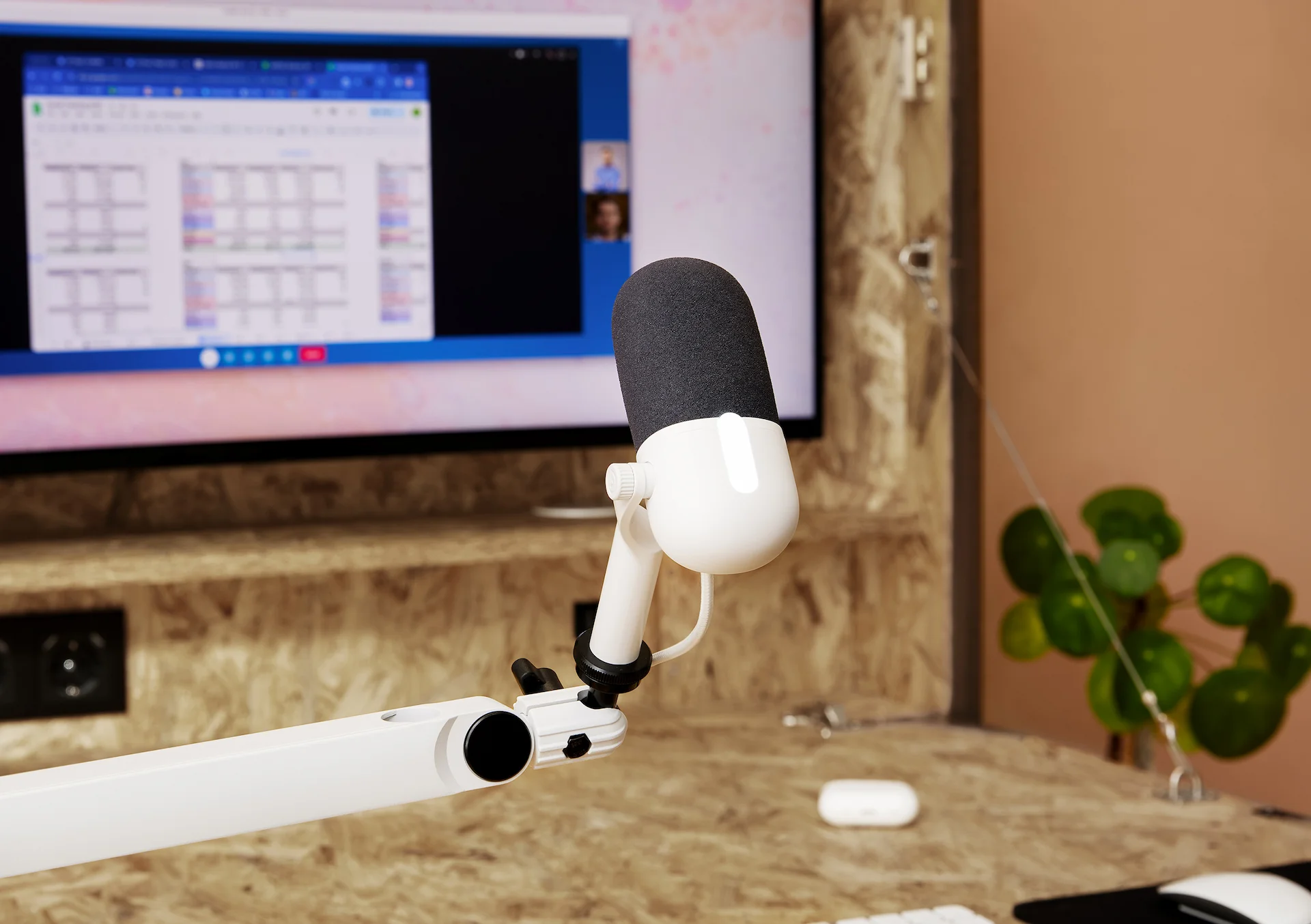 Mikrofon auf einem Ständer. Ein Monitor zeigt einen Videoanruf. Der Schreibtisch ist aus Holz.