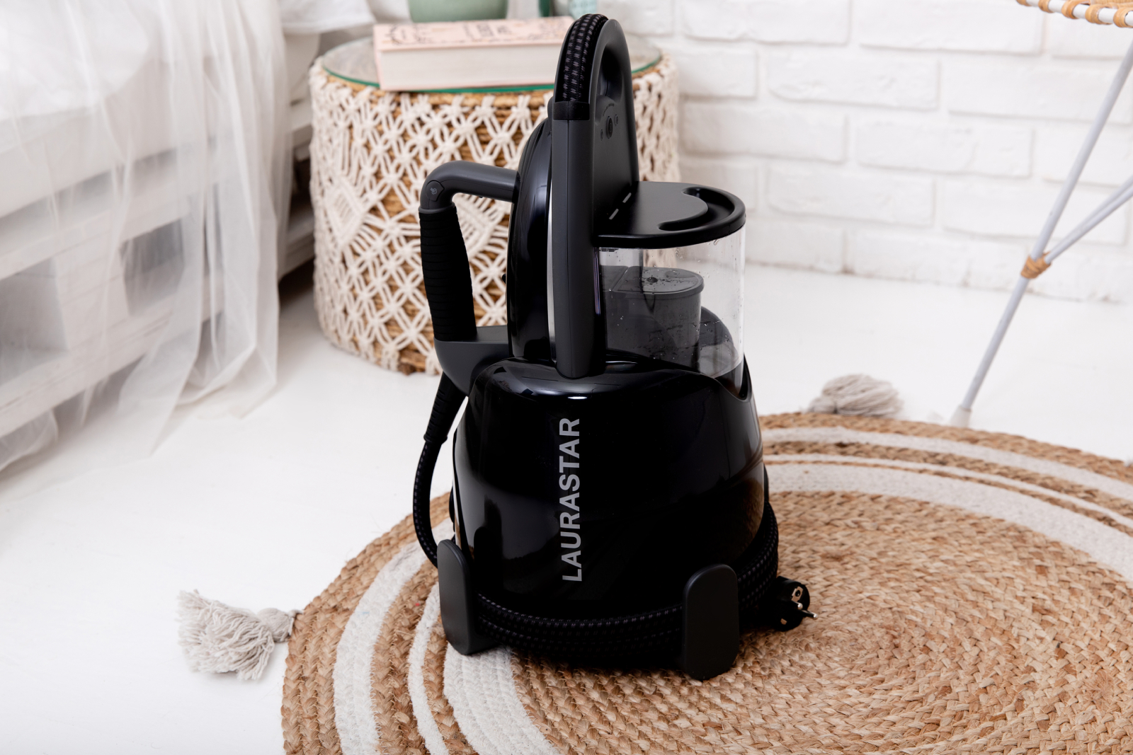 Czarny odkurzacz parowy na dywanie. Posiada czarny wąż i zbiornik na wodę.