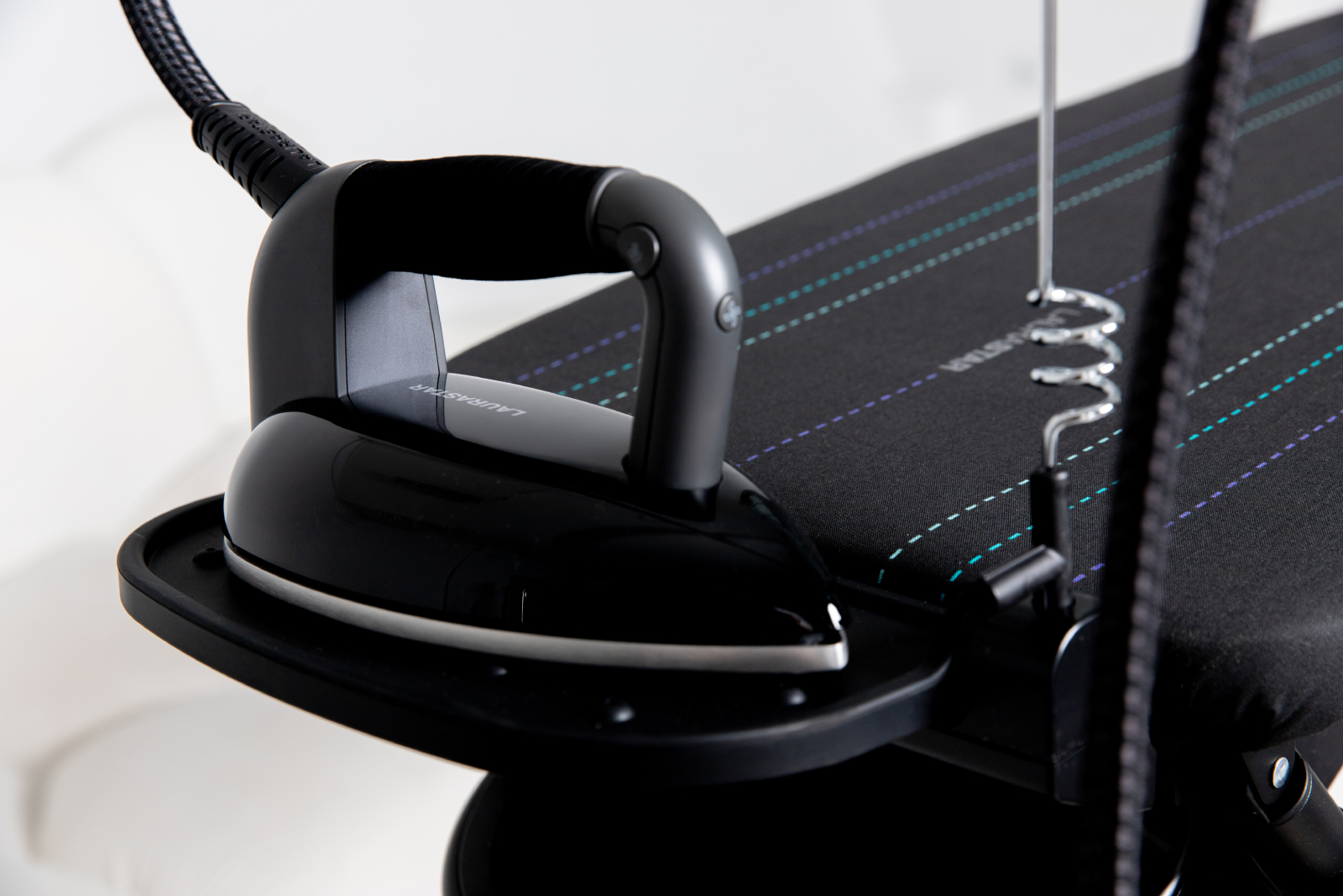 Czarne żelazko na czarnej desce do prasowania. Deska na białym tle. Uchwyt na parę z boku.