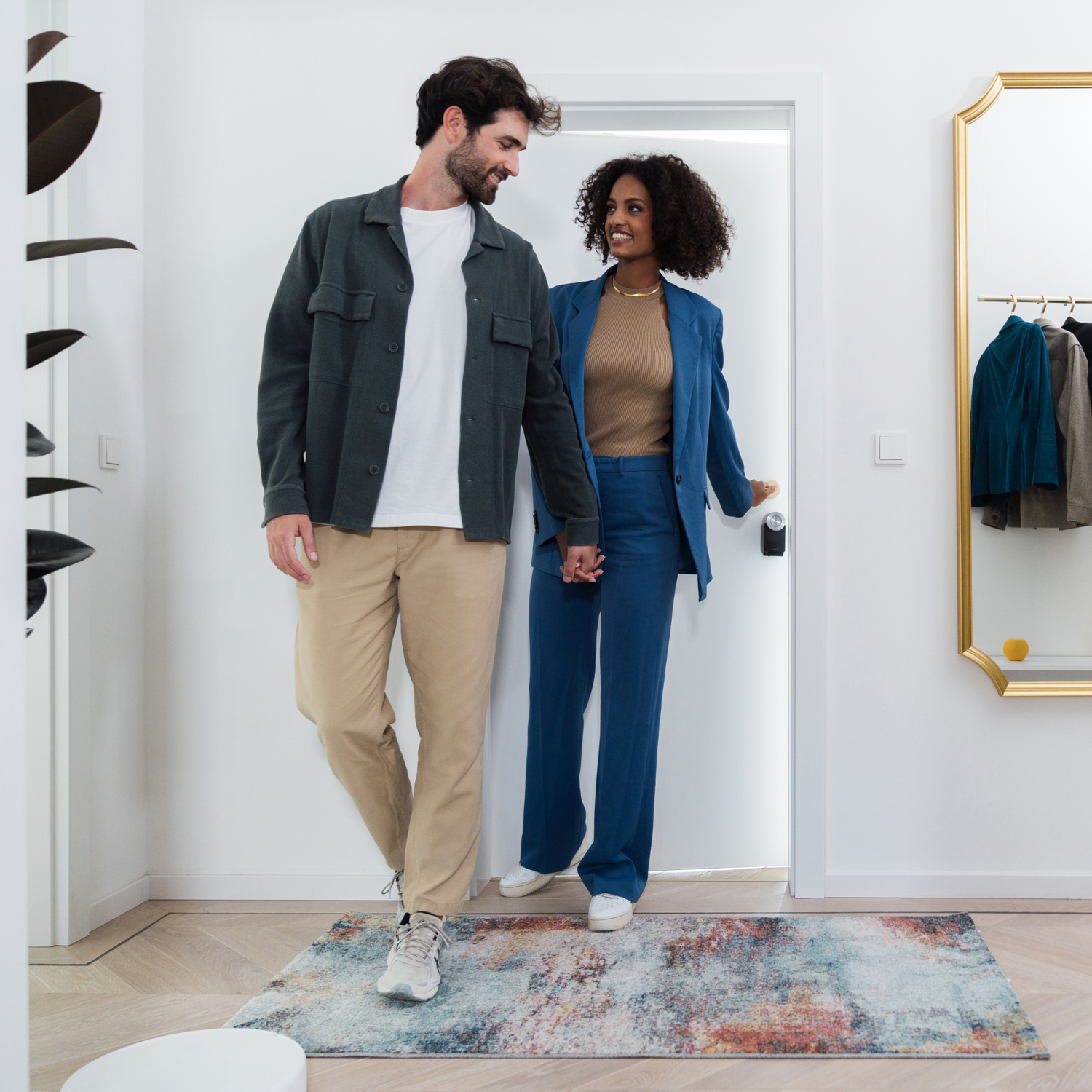 Couple holding hands, entering a home. A welcome mat and a mirror are visible.
