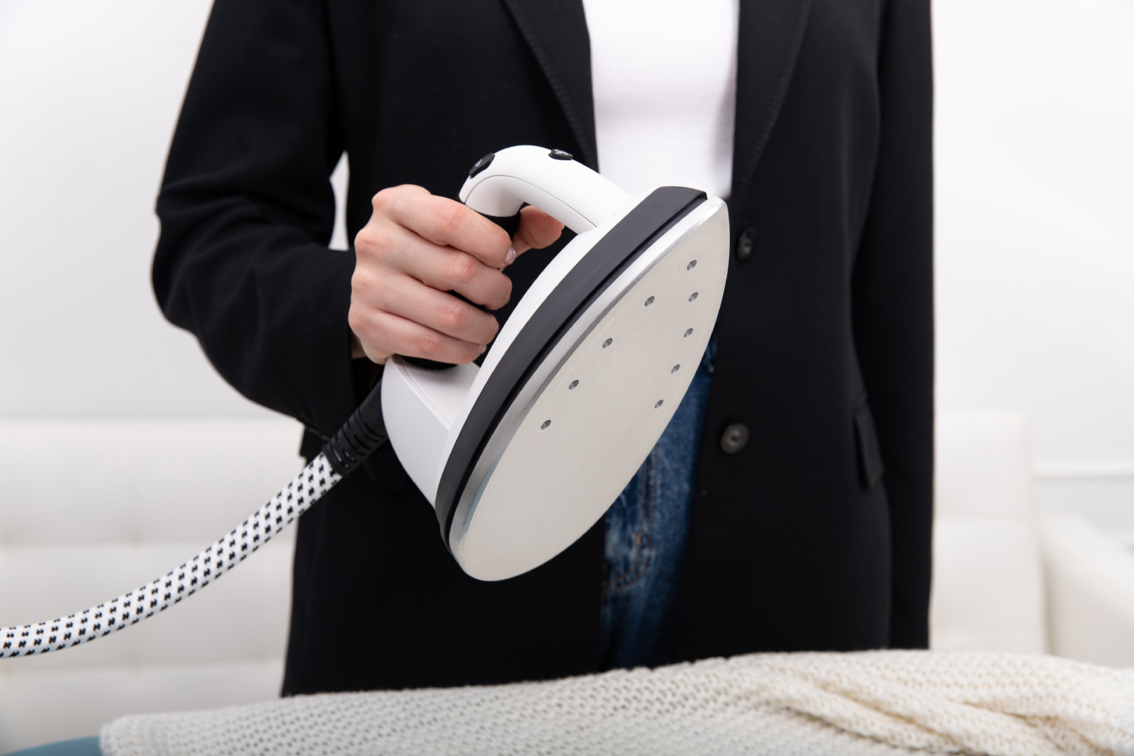 Osoba prasuje marynarkę na białej powierzchni z żelazkiem w dłoni.