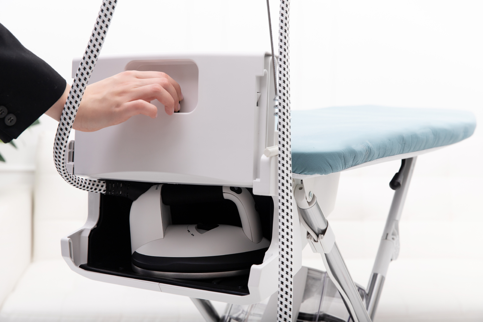 Ręka sięgająca do przegródki na białym stanowisku do prasowania, z żelazkiem i deską.