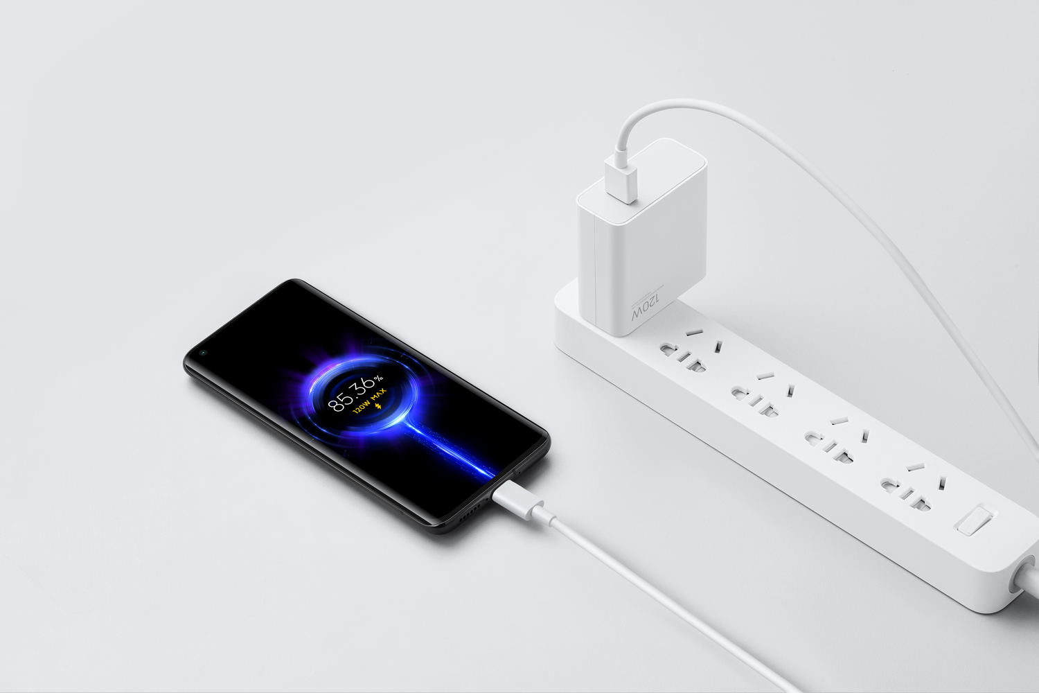 Un teléfono cargando, conectado a un ladrillo de carga blanco y una regleta. La pantalla del teléfono muestra un icono de carga.