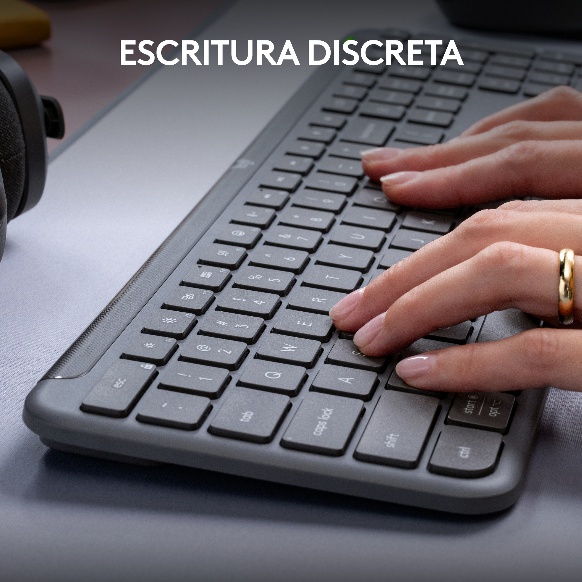 Manos escribiendo en un teclado gris oscuro, con el texto 'ESCRITURA DISCRETA'. Un anillo de oro en un dedo.