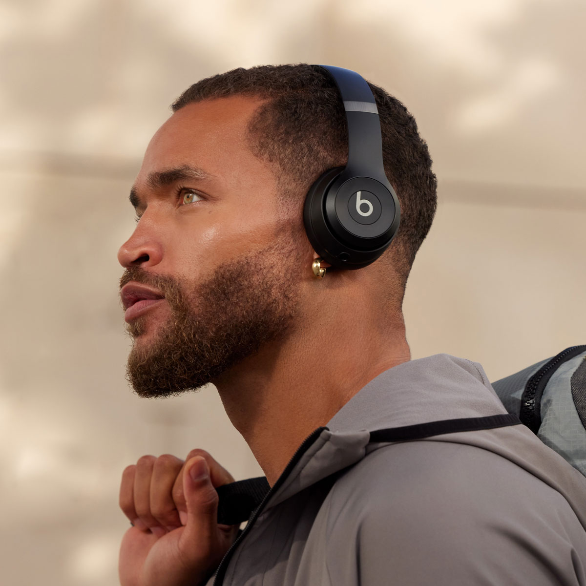 Hombre con auriculares Beats negros, mirando a la izquierda. Lleva una bolsa en el hombro.