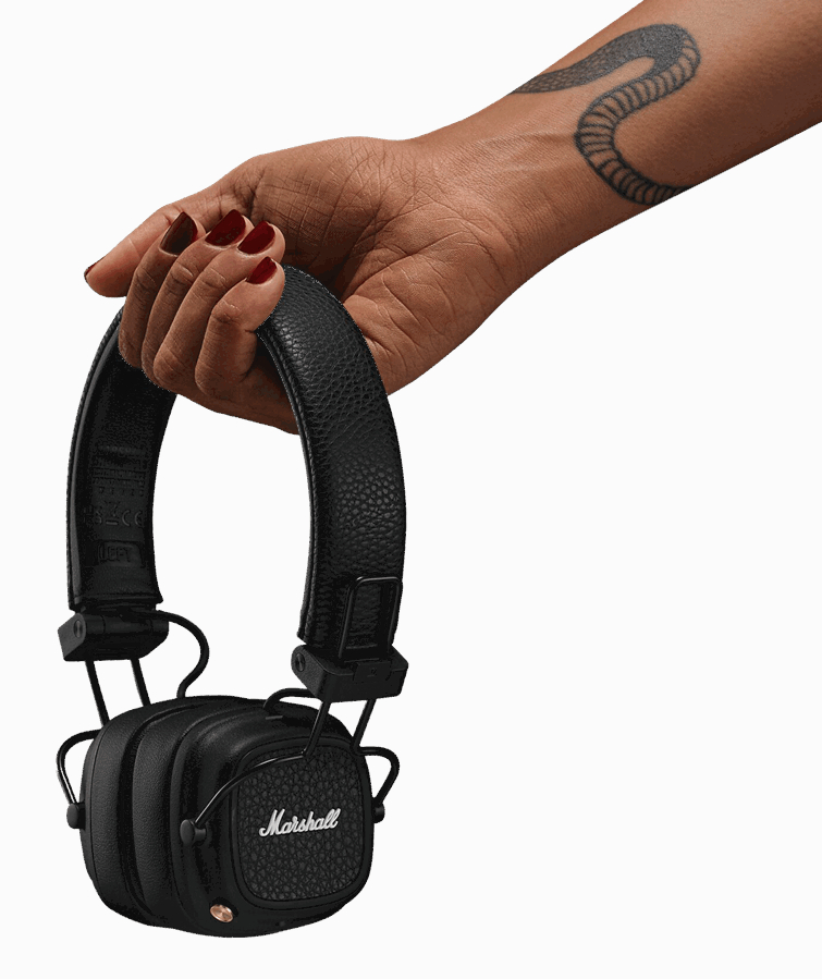 Dłoń trzymająca czarne słuchawki Marshall, czerwony lakier do paznokci i tatuaż.