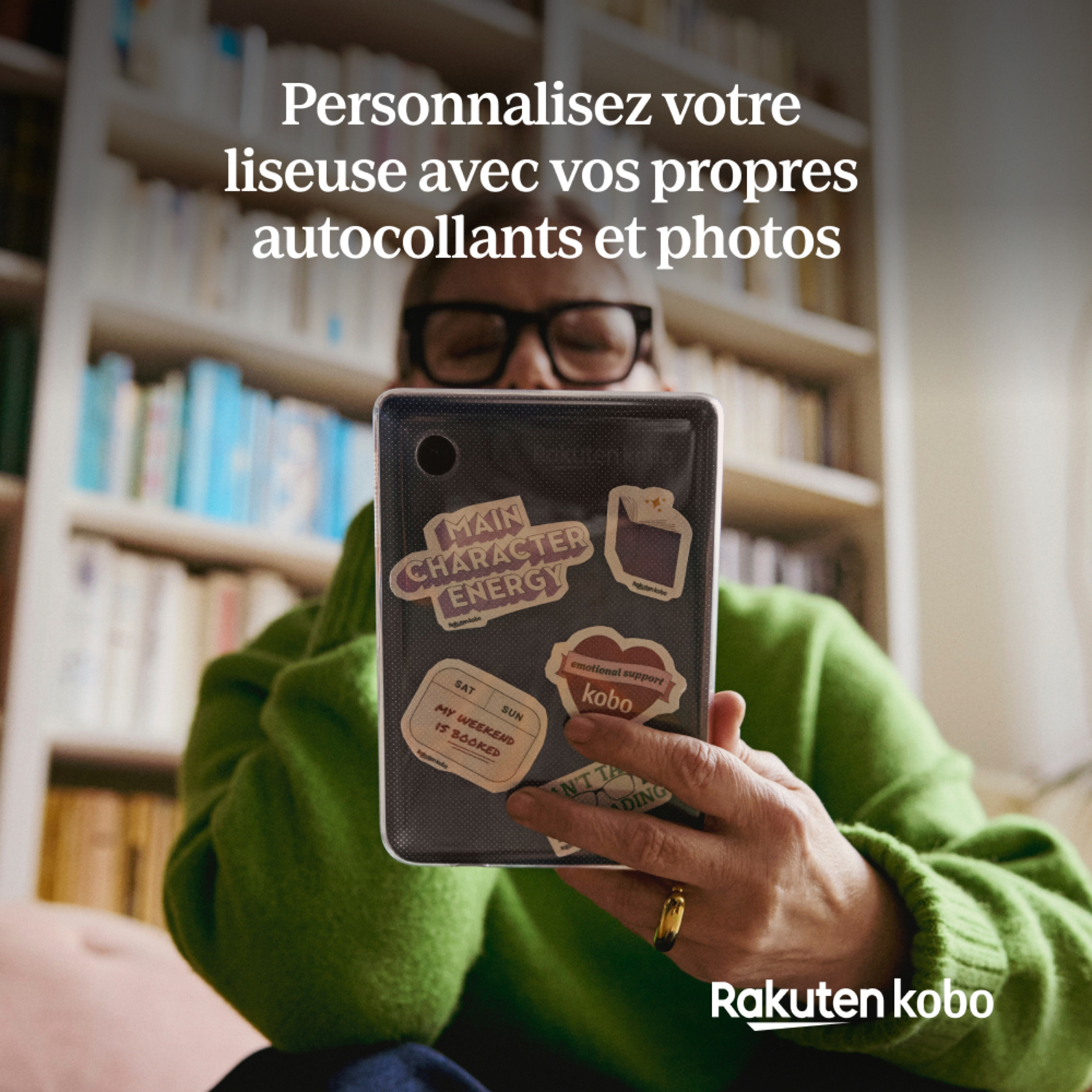 Personne tenant une tablette avec des autocollants, entourée de bibliothèques.