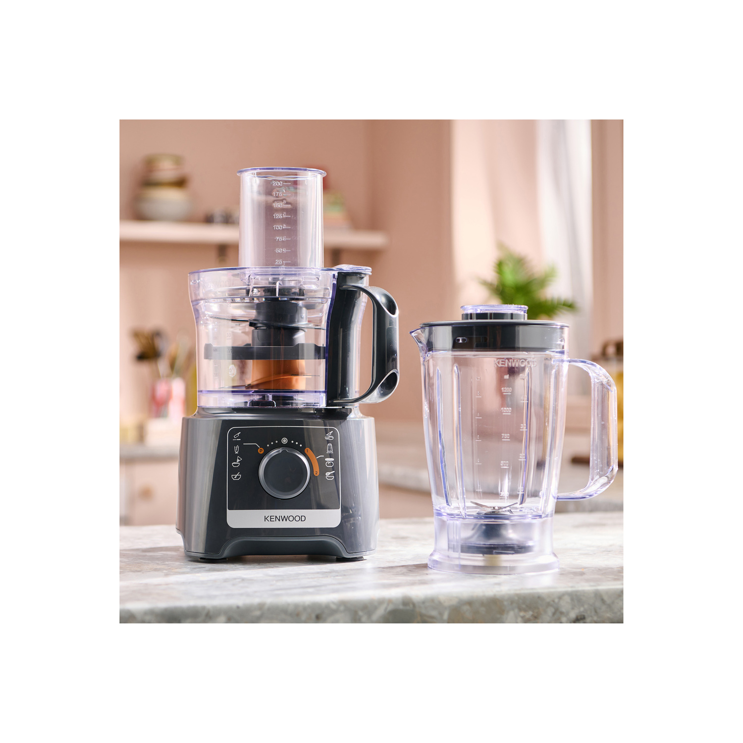 Un robot culinaire Kenwood gris foncé avec un mixeur à droite, sur une surface en marbre.