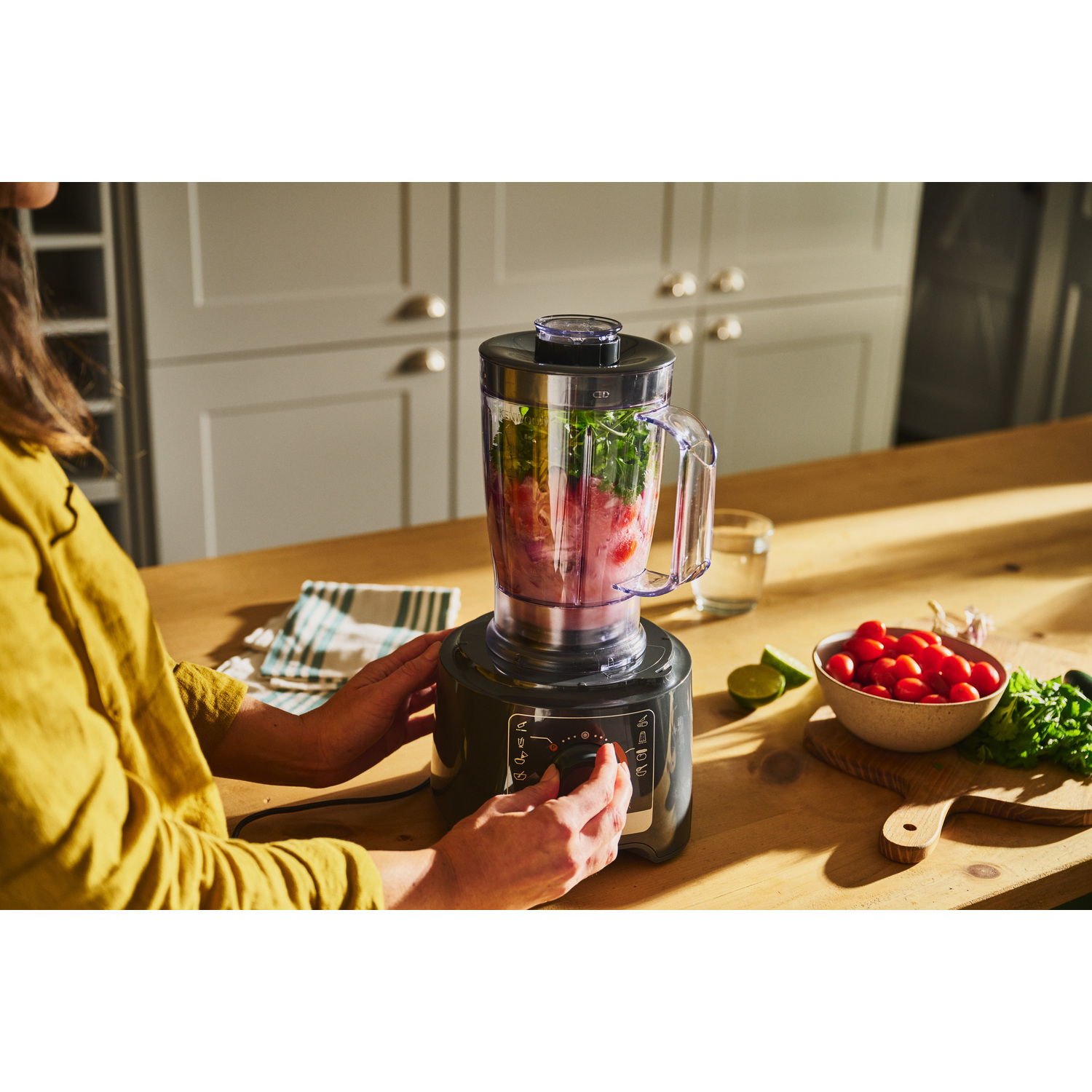 Mixeur avec ingrédients, mains de femme le tenant, entouré d'ingrédients.