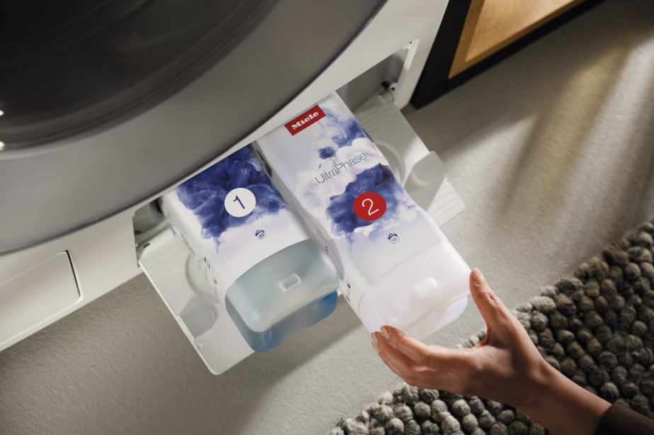 Pralka z dwoma wkładami na detergent oznaczonymi 1 i 2, ręka sięga po jeden.