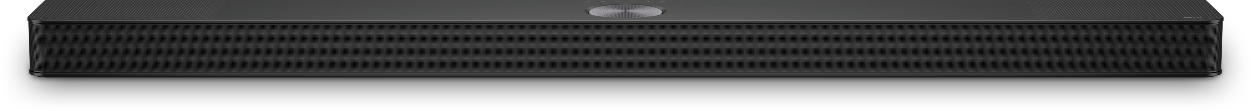 Eine lange, schwarze Soundbar mit zentralem Bedienknopf, platziert auf einer weißen Oberfläche. Einfaches Design.