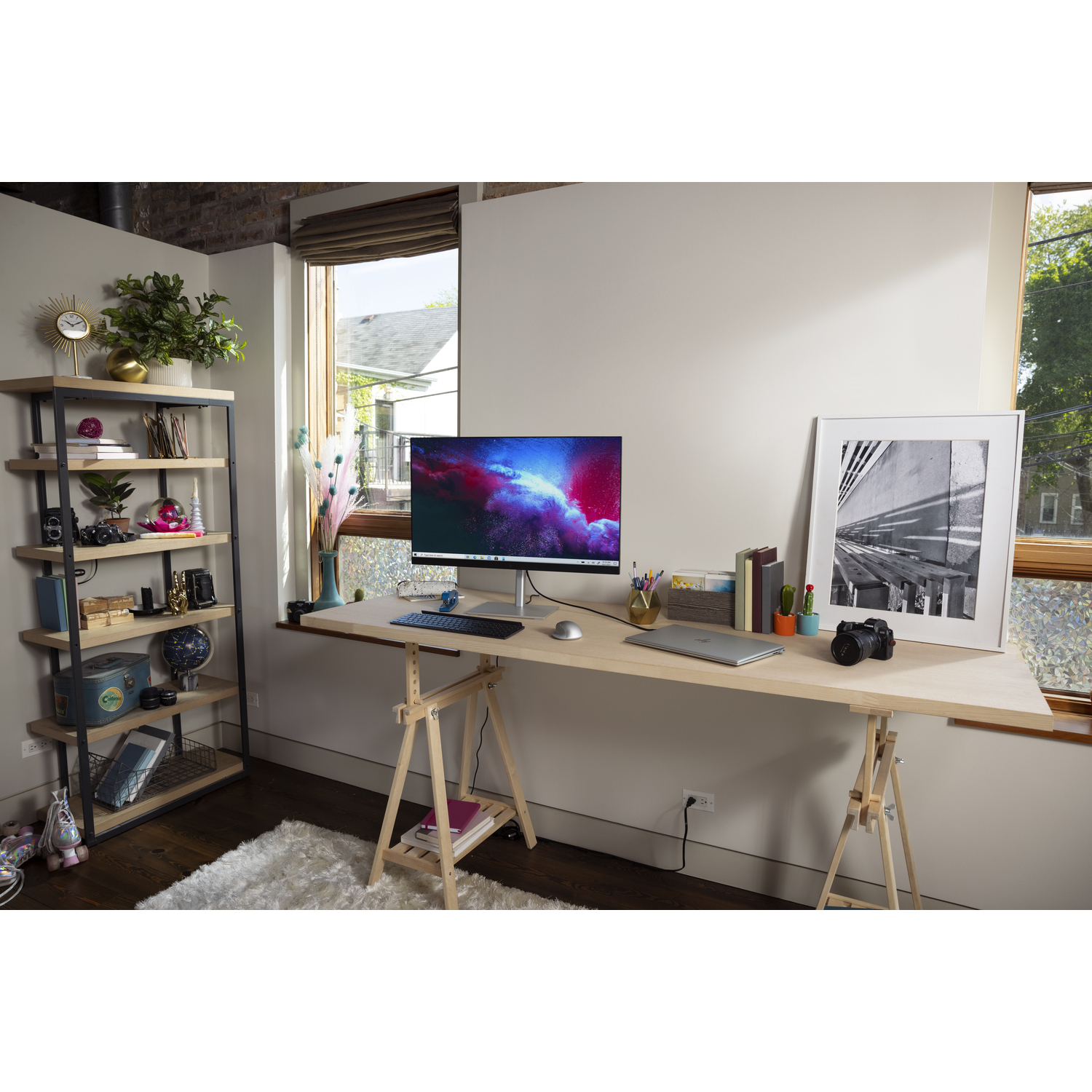Desk setup with monitor, keyboard, and laptop. Bookshelf and window in the background.