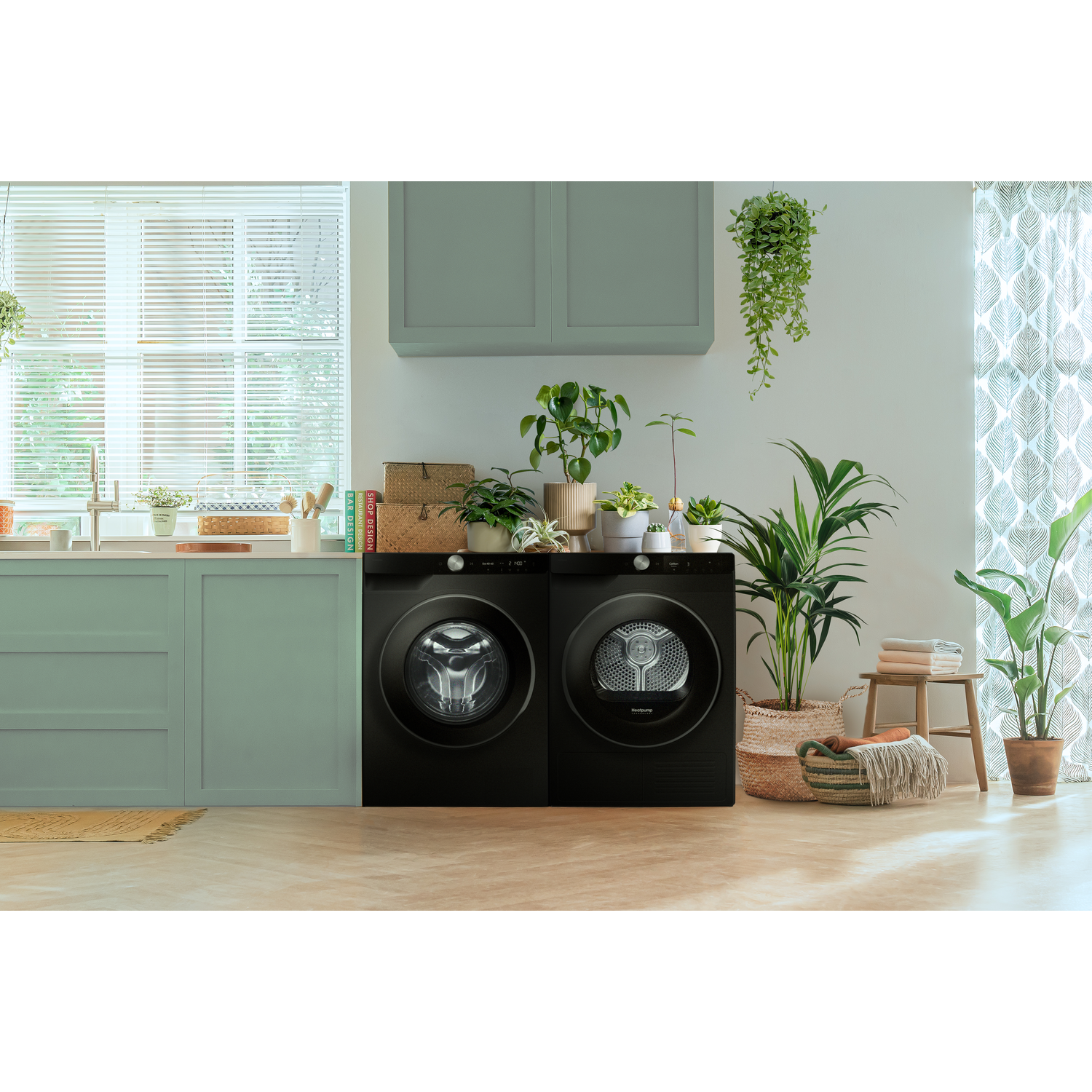 Black washing machine and dryer in a laundry room. Plants and decor around the appliances.