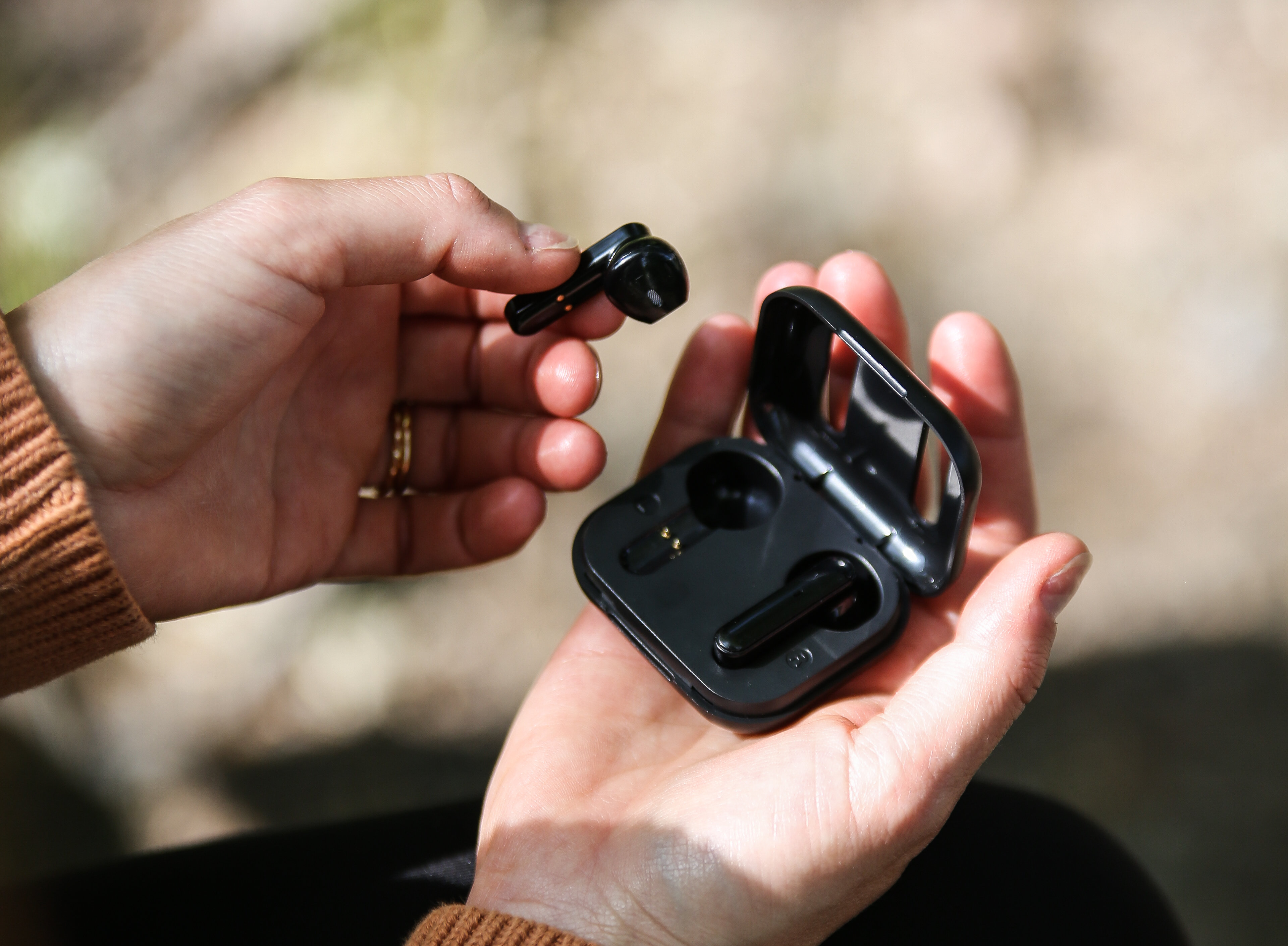 Dłoń trzymająca czarne bezprzewodowe słuchawki i etui.