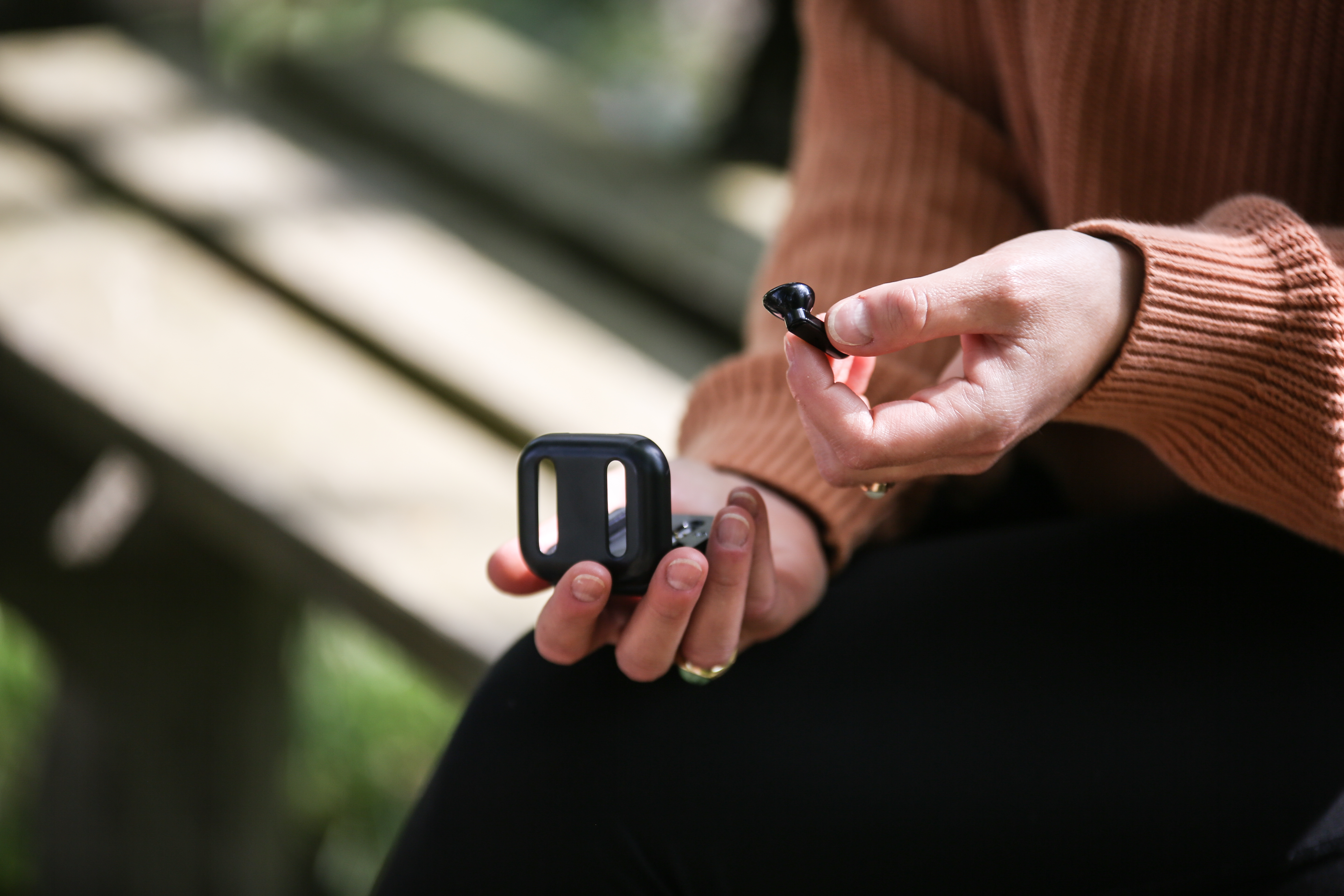 Dłonie osoby trzymającej czarną słuchawkę i etui ładujące na zewnątrz.