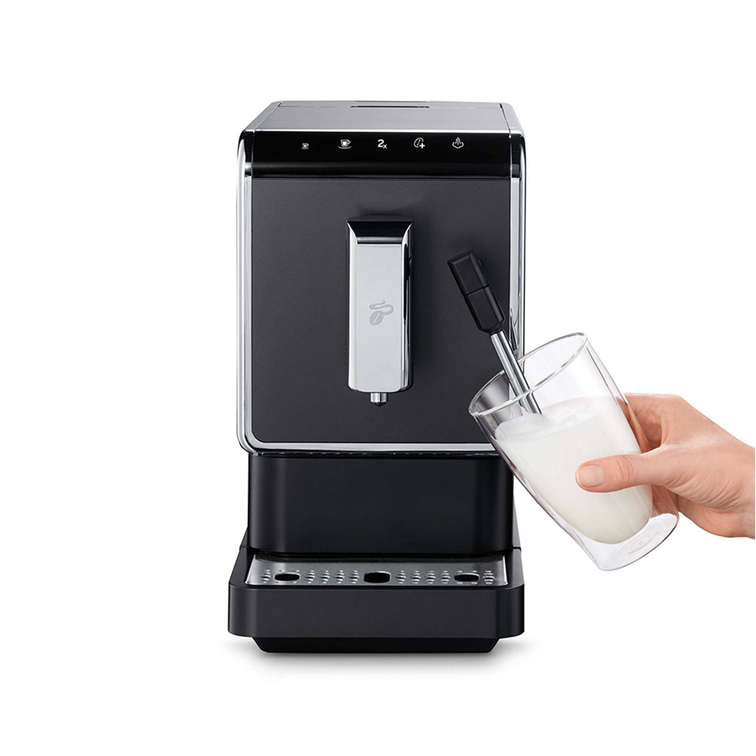 Eine schwarz-silberne Espressomaschine, eine Person gießt Milch in ein Glas, vor weißem Hintergrund.