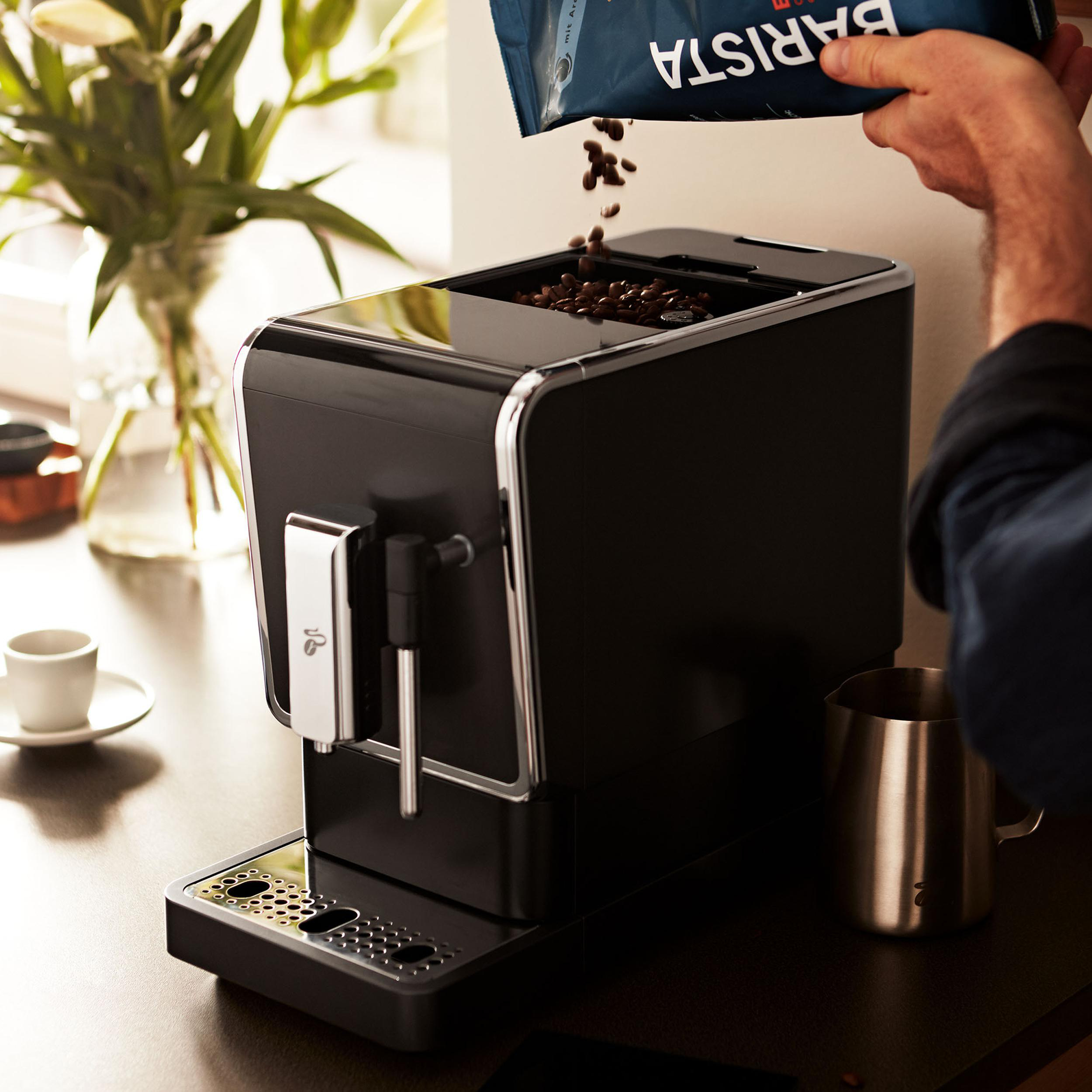 Eine Person gießt Kaffeebohnen in eine schwarze Kaffeemaschine.