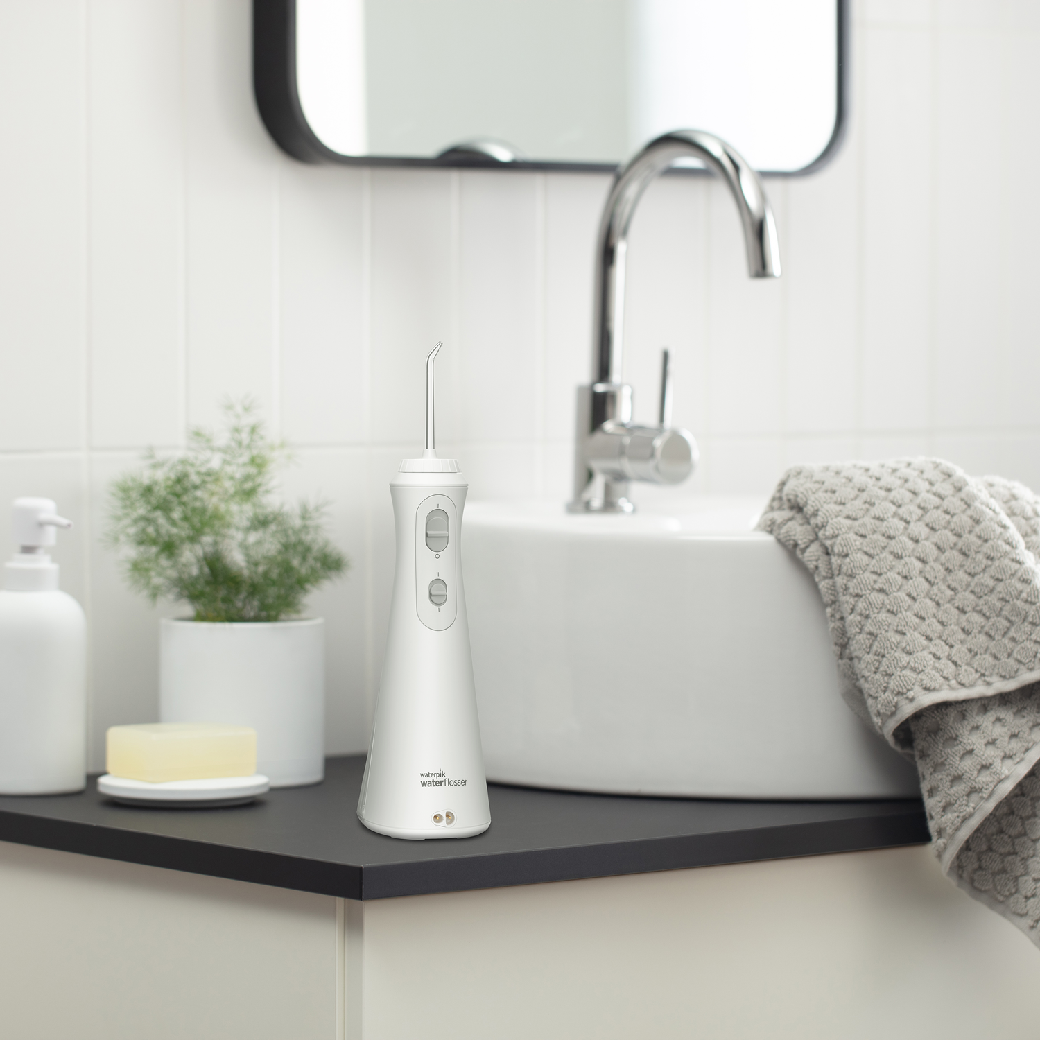 Witte waterflosser op een zwart aanrecht in een badkamer met spiegel.