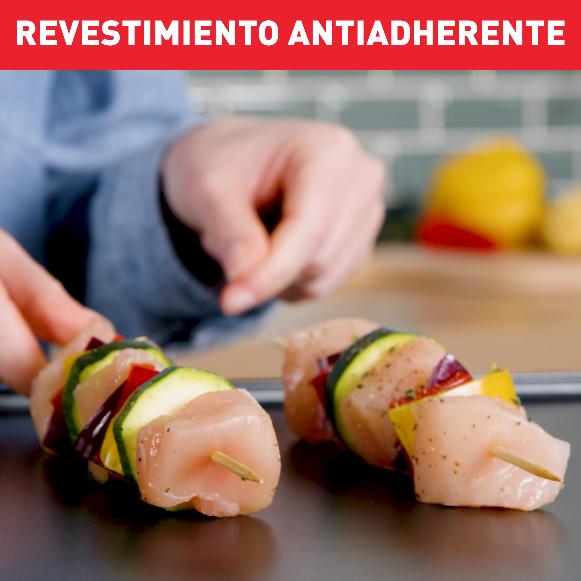 Manos preparando brochetas con pollo, calabacín y cebolla roja. La palabra 'Revestimiento antiadherente' está escrita en rojo.