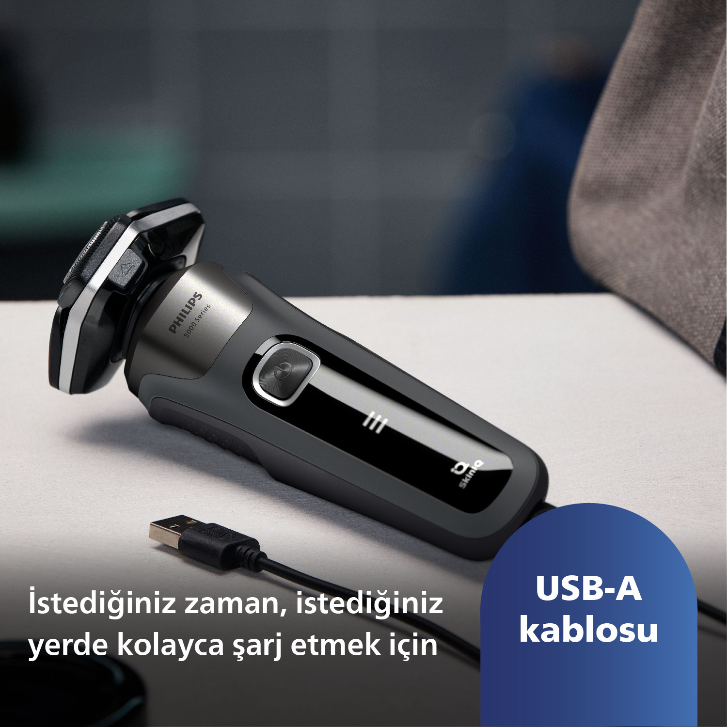 Siyah ve gümüş elektrikli tıraş makinesi, beyaz bir yüzeyde USB-A kablosu takılı.