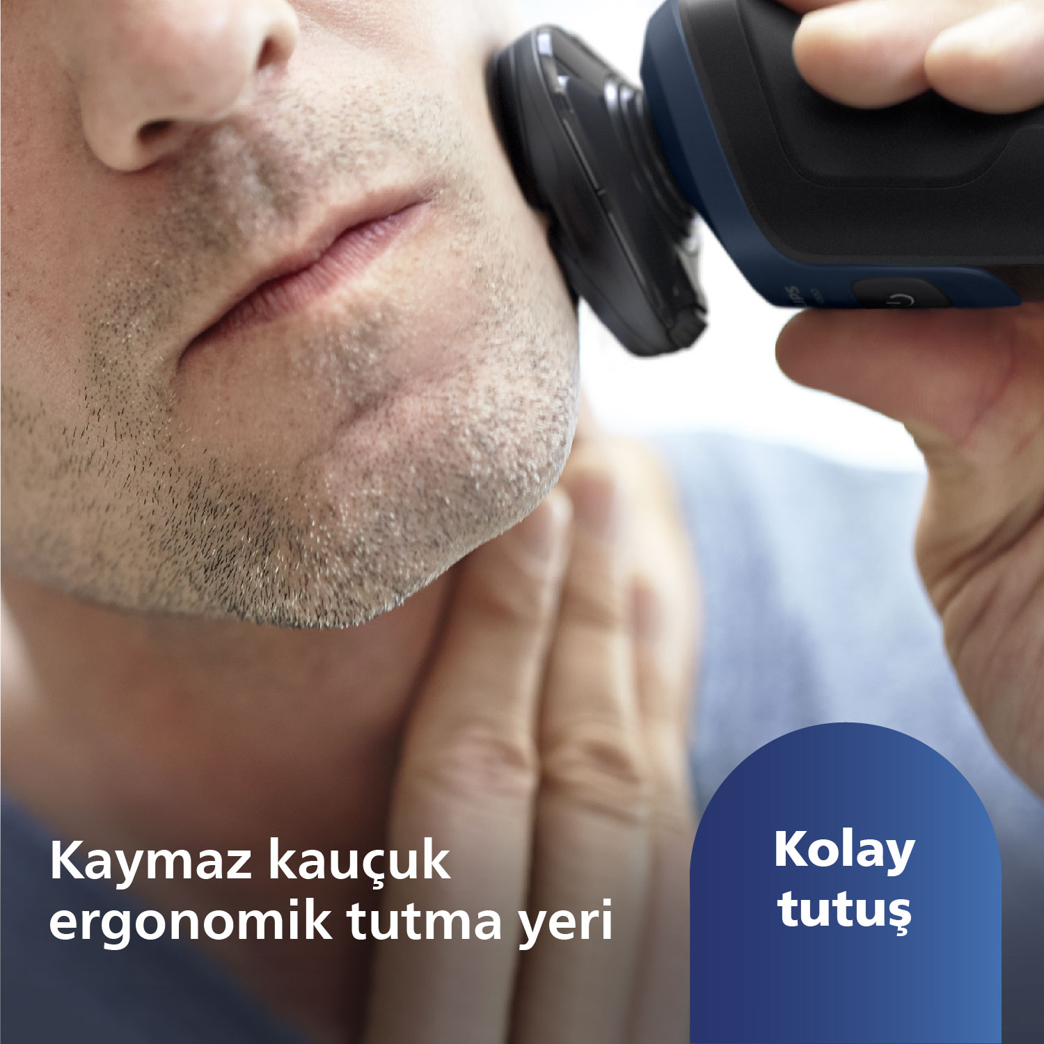 Bir adam siyah ve mavi bir elektrikli tıraş makinesiyle sakalını tıraş ediyor, yakın çekim.