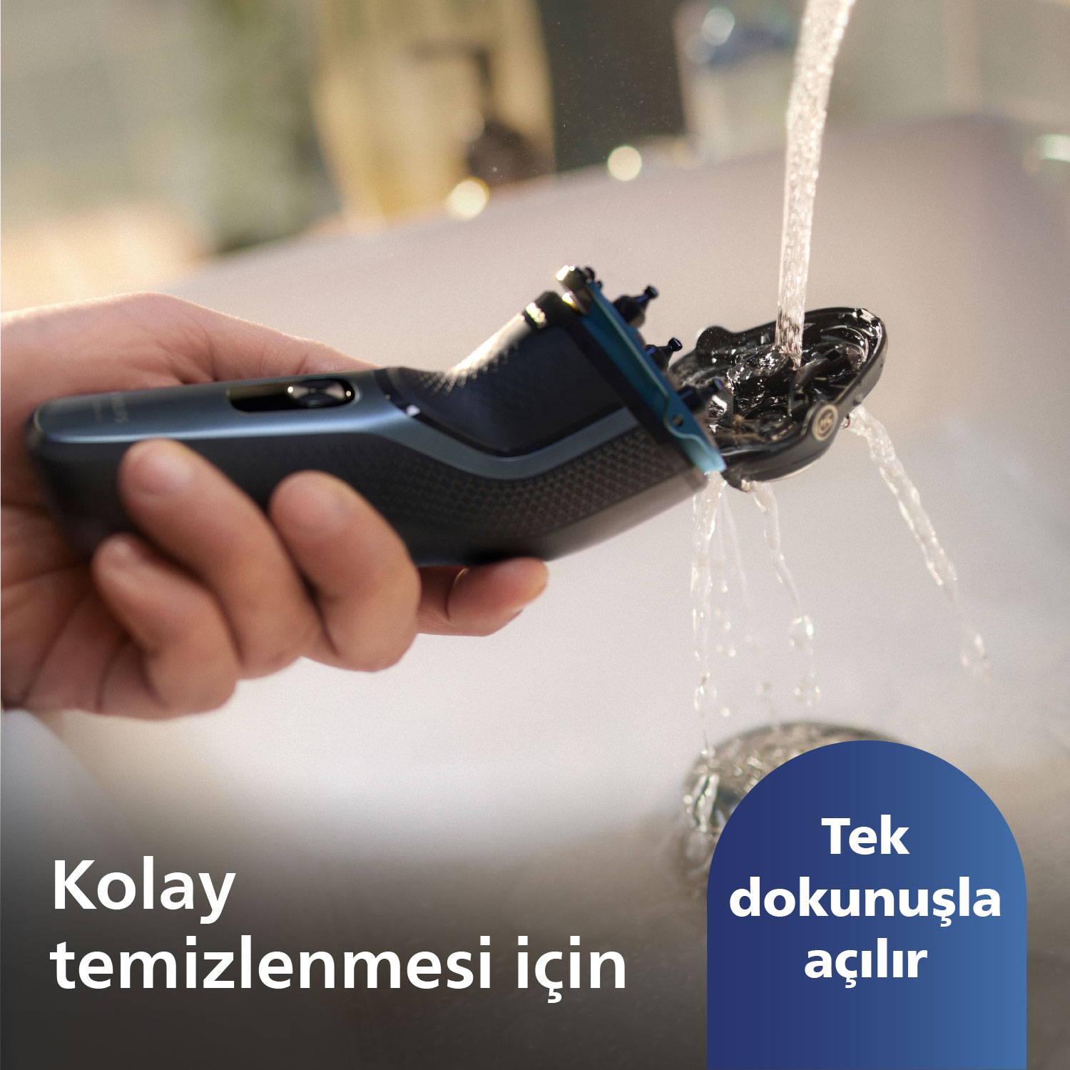 Bir el, temizlemek için akan suyun altında mavi bir elektrikli tıraş makinesi tutuyor.