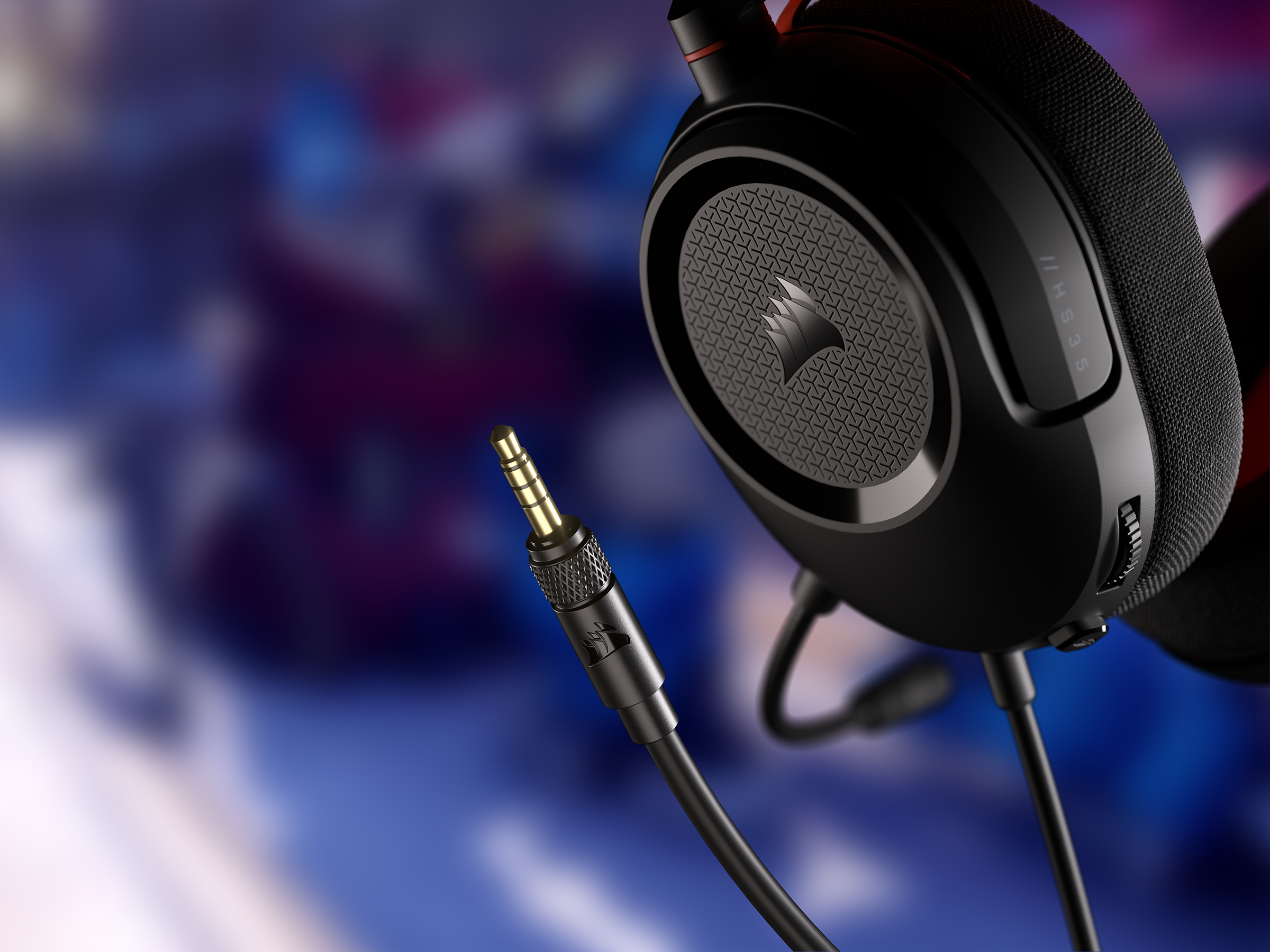 Schwarze Corsair HS35 Kopfhörer mit schwarzem Kabel und vergoldetem Stecker. Der Hintergrund ist farbig verschwommen.