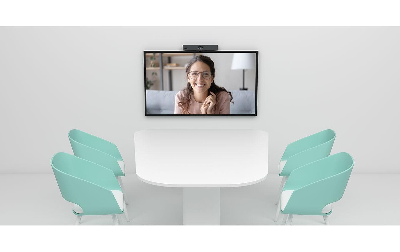 Ein weißer Konferenztisch mit vier mintgrünen Stühlen steht vor einer Wand mit einem Bildschirm für Videokonferenzen.