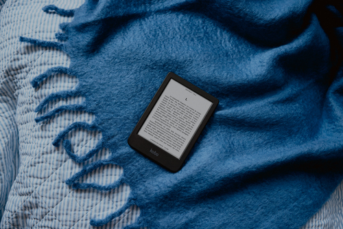 E-Reader auf einer blauen Decke. Der Bildschirm zeigt Text. Weißer und blau gestreifter Hintergrund.