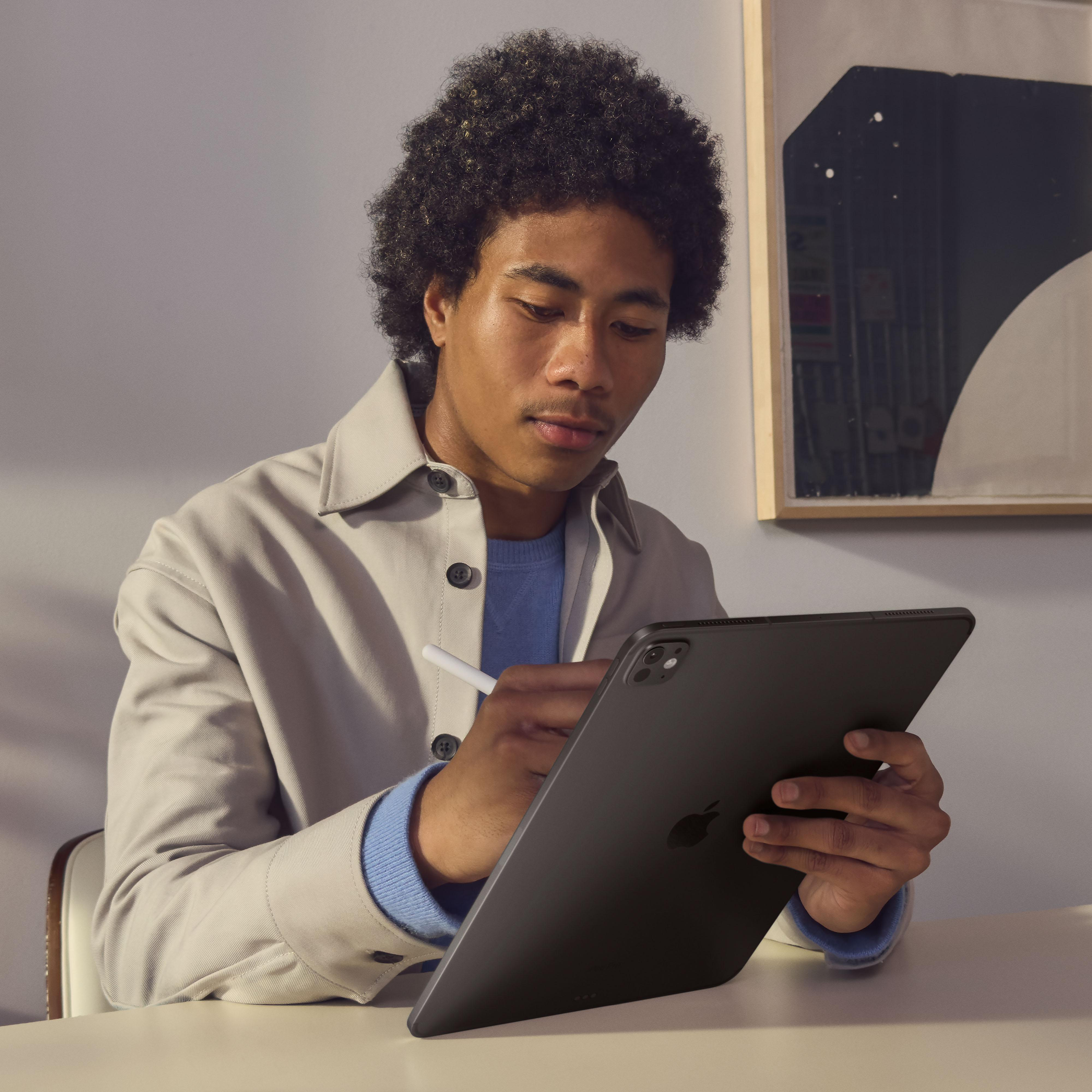 Ein Mann mit dunklem Haar und einer hellen Jacke benutzt ein Tablet mit Stift an einem Tisch. Ein Gemälde hängt an der Wand.