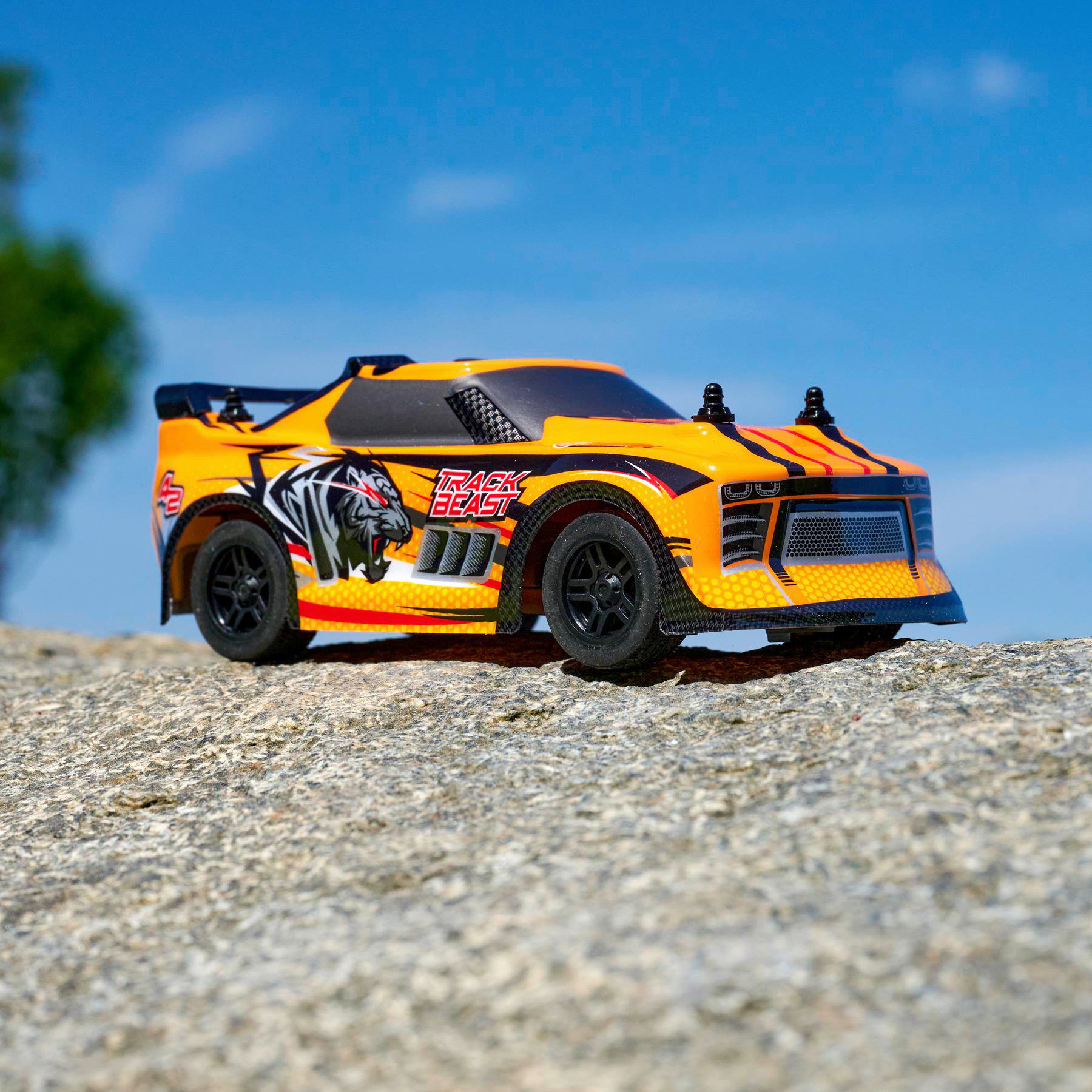 Ein gelbes Spielzeugauto mit schwarzen Rädern auf einer rauen Steinoberfläche, unter blauem Himmel.