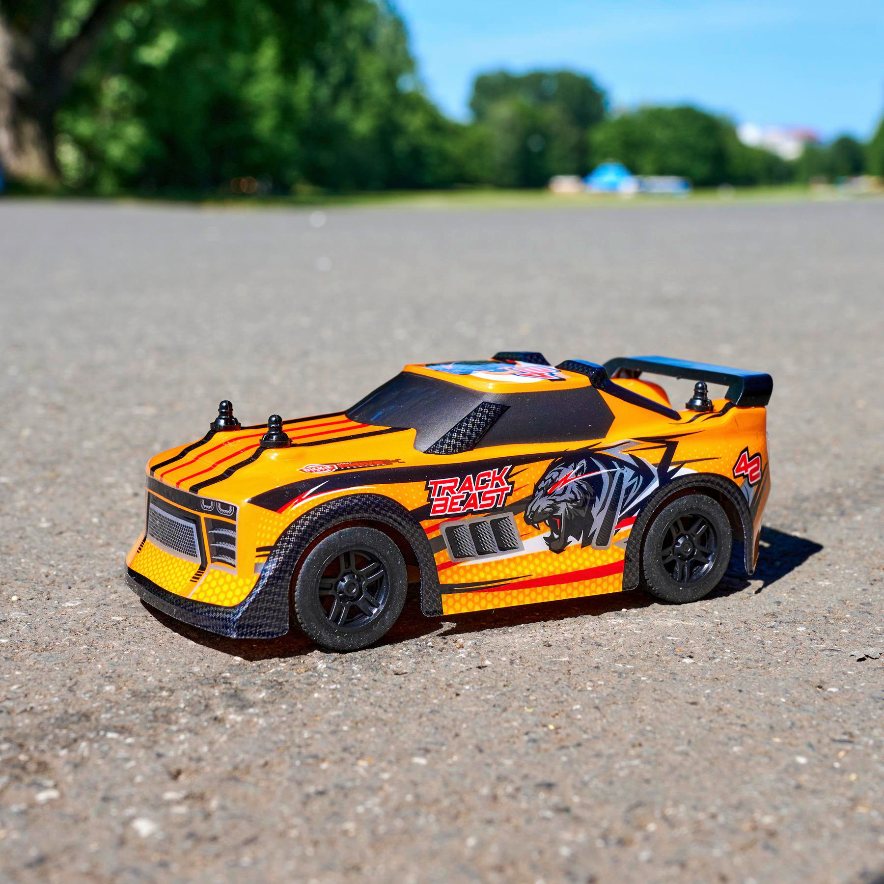 Ein orange-schwarzes Spielzeug-Rennauto auf grauer Oberfläche, in sonniger Umgebung.
