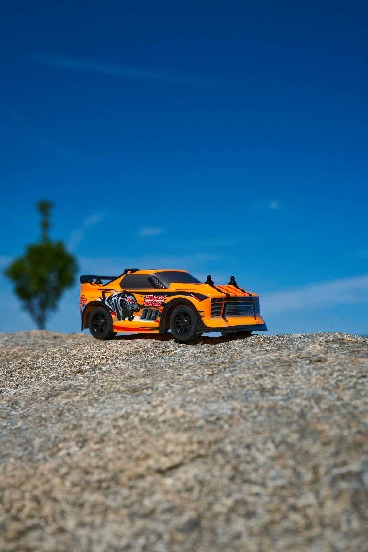 Orangefarbenes Spielzeugauto auf Felsen mit blauem Himmel im Hintergrund.