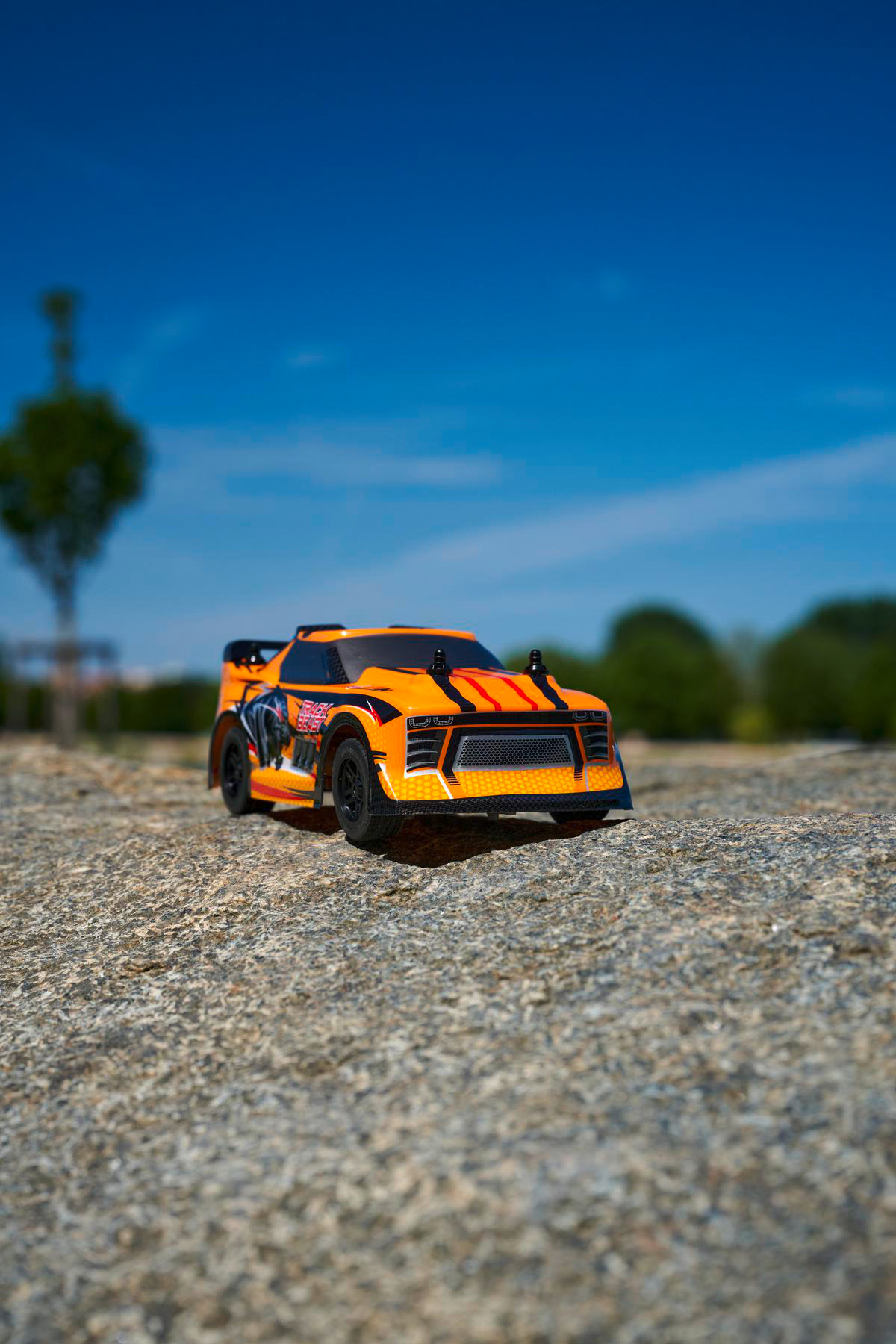 Ein orangefarbenes RC-Auto auf einer Steinoberfläche vor blauem Himmel.