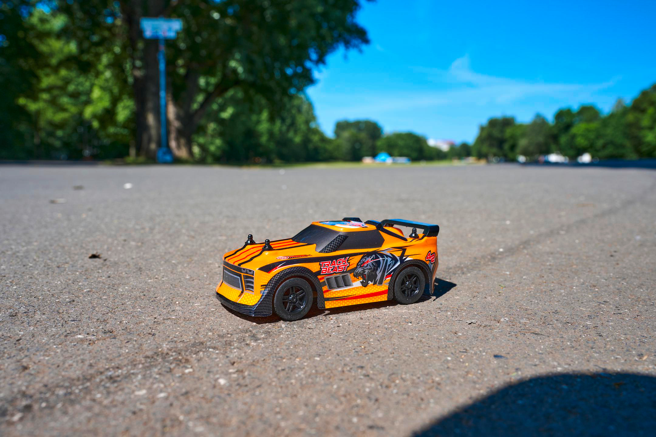Ein orangefarbenes Spielzeug-Rennauto steht mitten auf einer grauen, gepflasterten Straße.