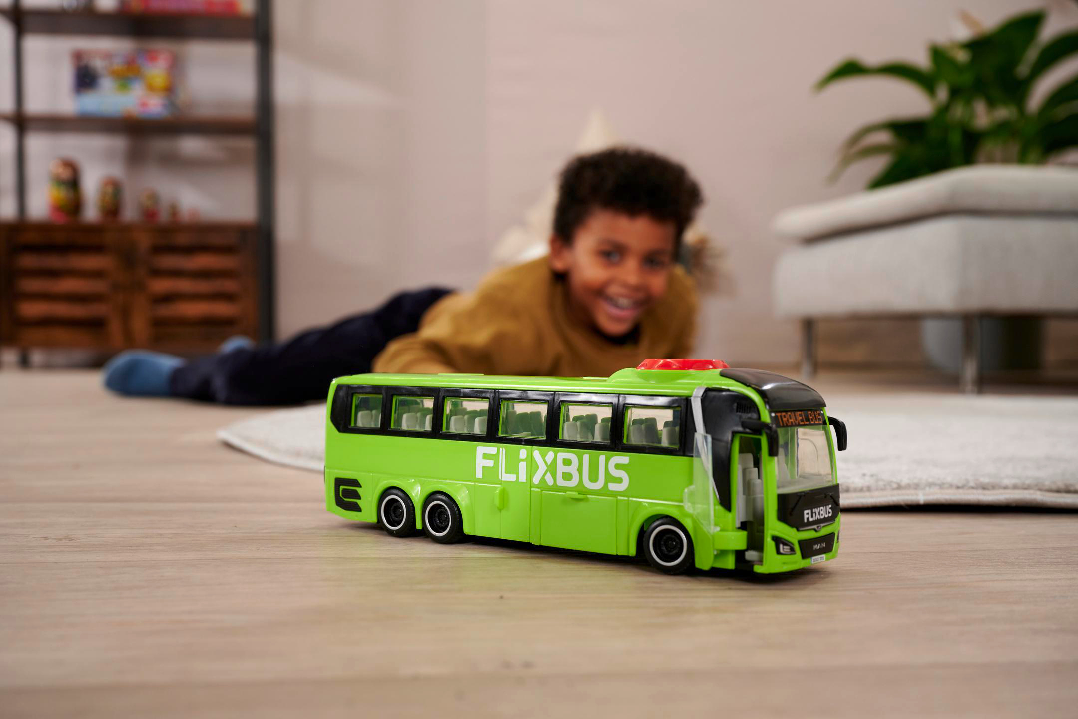 Ein Junge lächelt und spielt mit einem grünen Spielzeugbus. Der Bus hat den Namen 'Flixbus'.