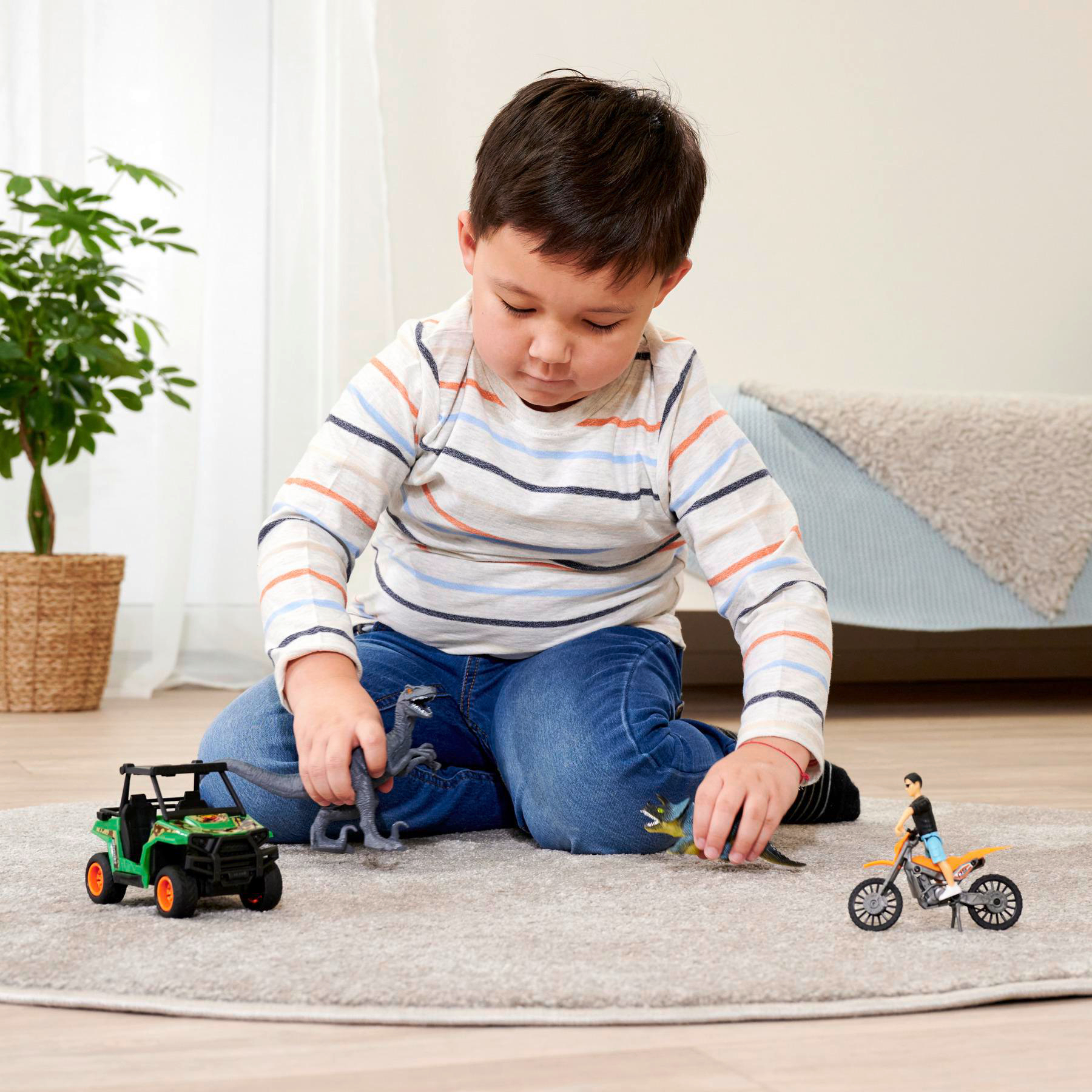 Ein Kind spielt mit Spielzeugdinosauriern, einem Motorrad und einem Jeep auf einem Teppich.