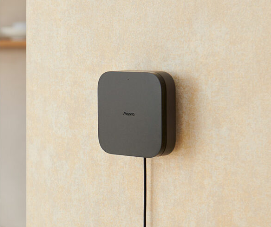Un appareil carré gris est monté sur un mur beige. Un câble noir y est connecté.