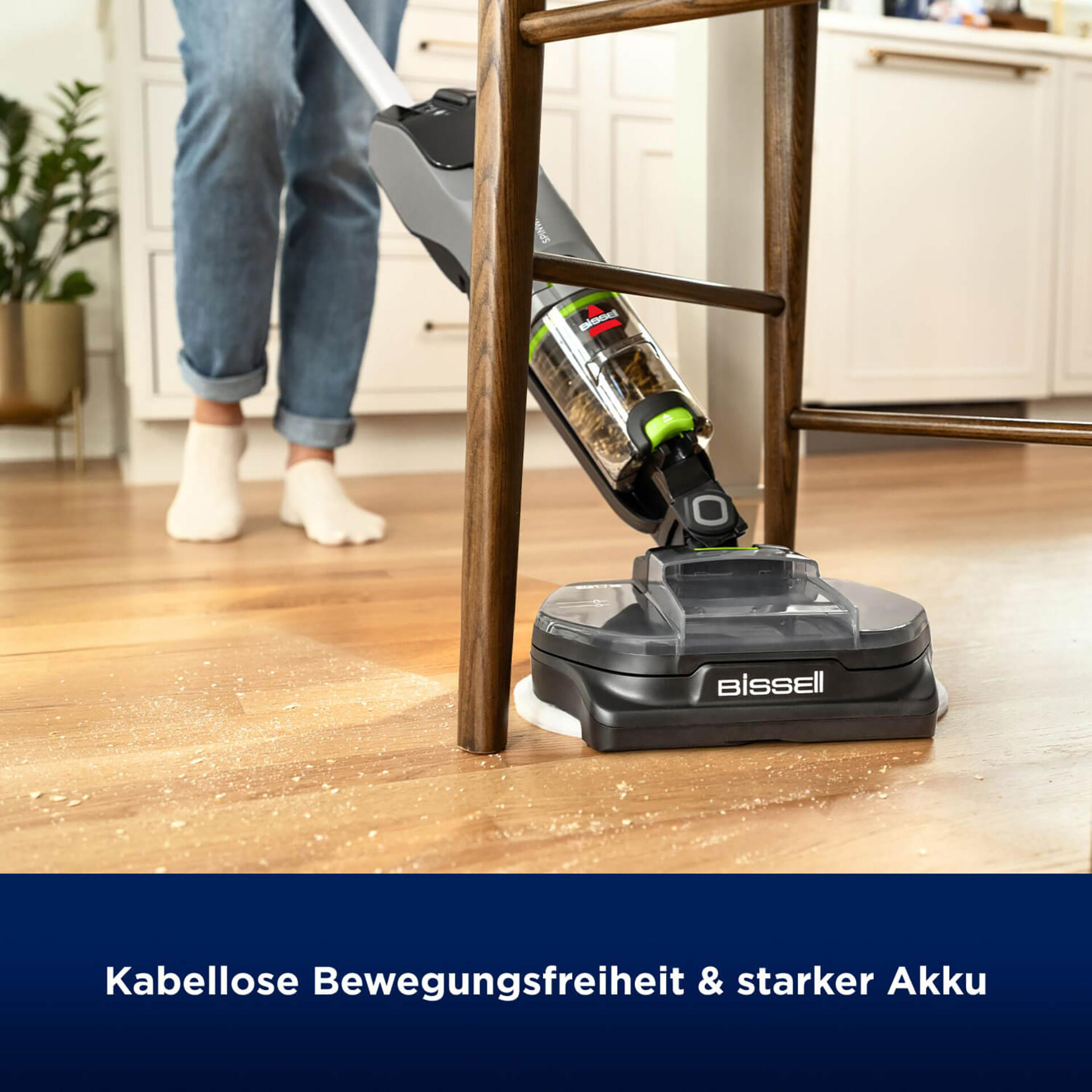 Eine Frau saugt einen Holzboden mit einem kabellosen Staubsauger. Holzspäne sind sichtbar.